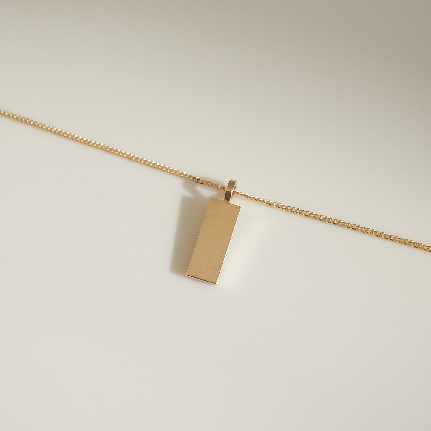 Minimalist gold rectangular pendant on a delicate chain displayed on a light background, highlighting luxury jewellery elegance.