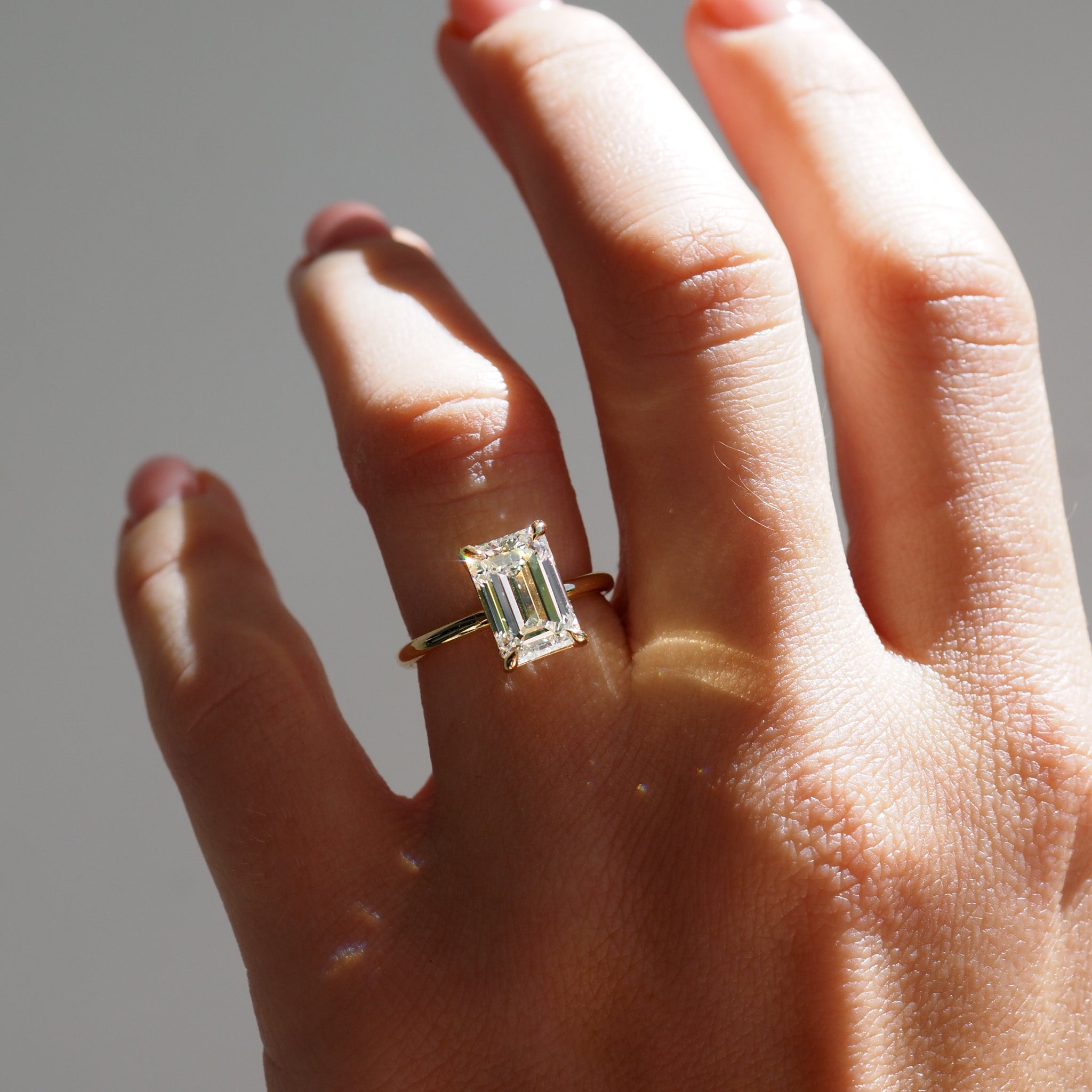 Hand wearing an emerald cut diamond on a yellow gold band