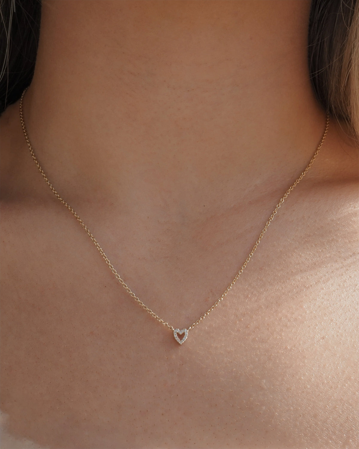 A delicate gold chain necklace with a small heart-shaped pendant featuring hand set lab grown diamonds, shown worn on a model's neck.