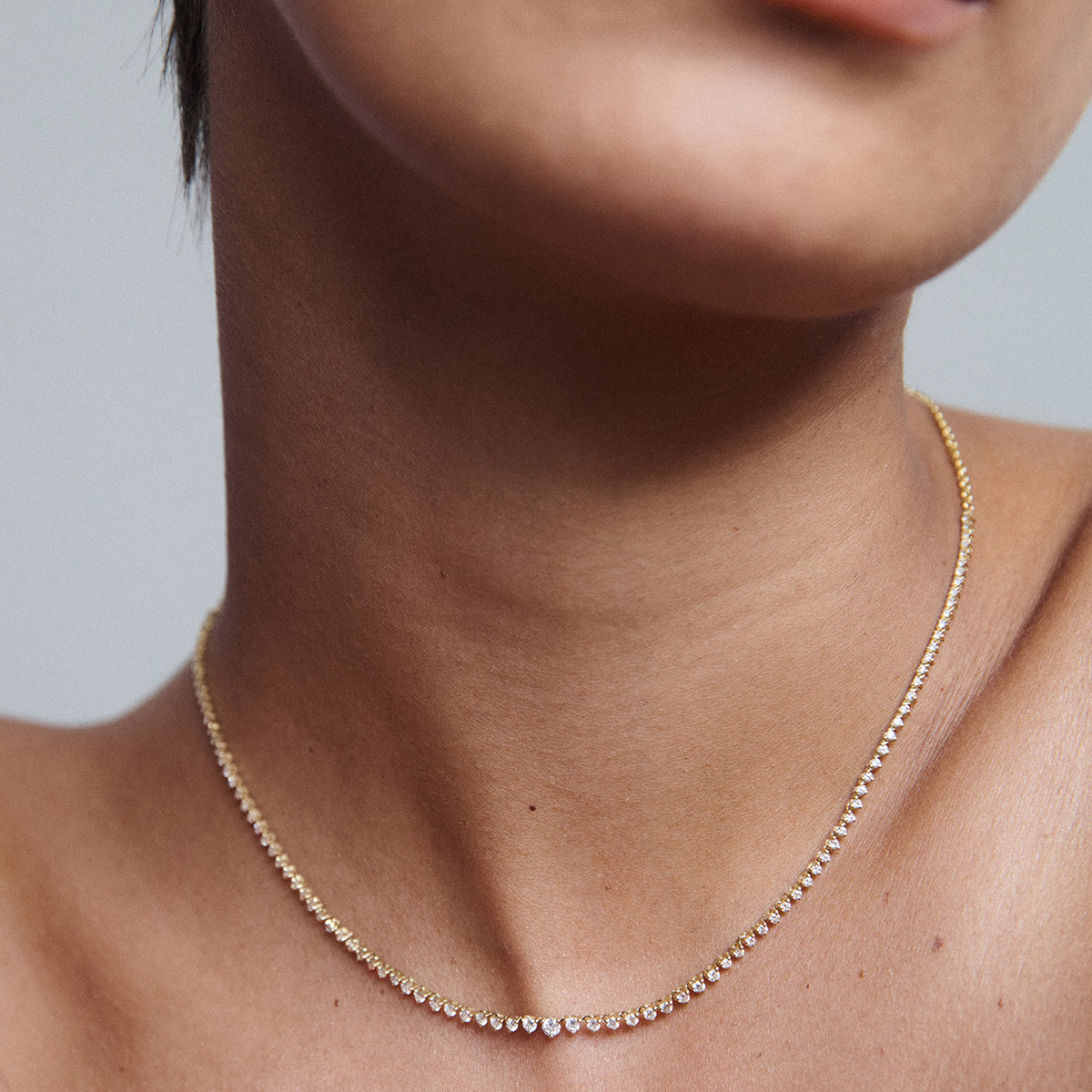 Close-up of a woman wearing a delicate gold necklace with small, sparkling diamonds. High-end jewellery, luxury fashion.