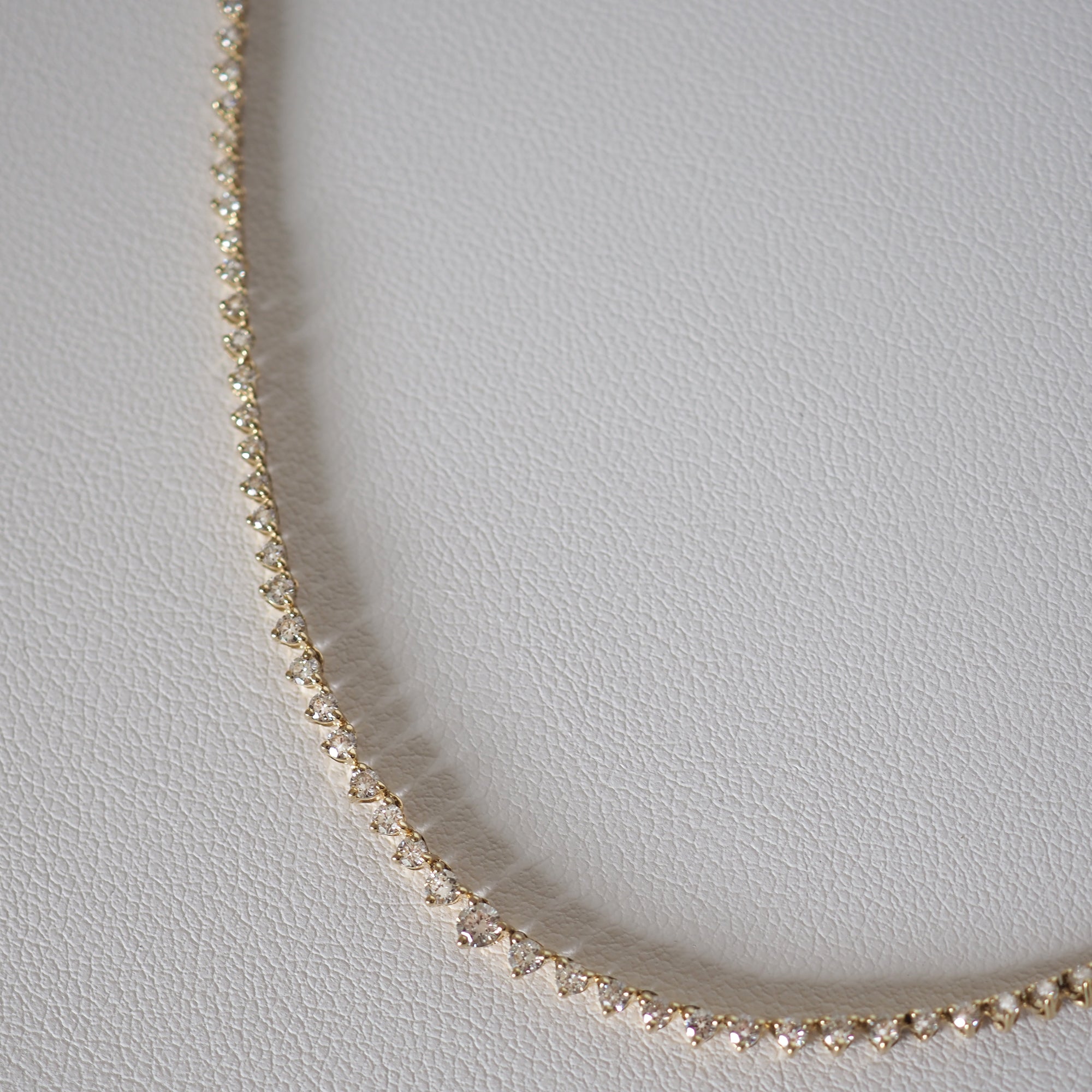 Gold diamond tennis necklace on a white leather surface, showcasing elegant, luxury jewellery design.