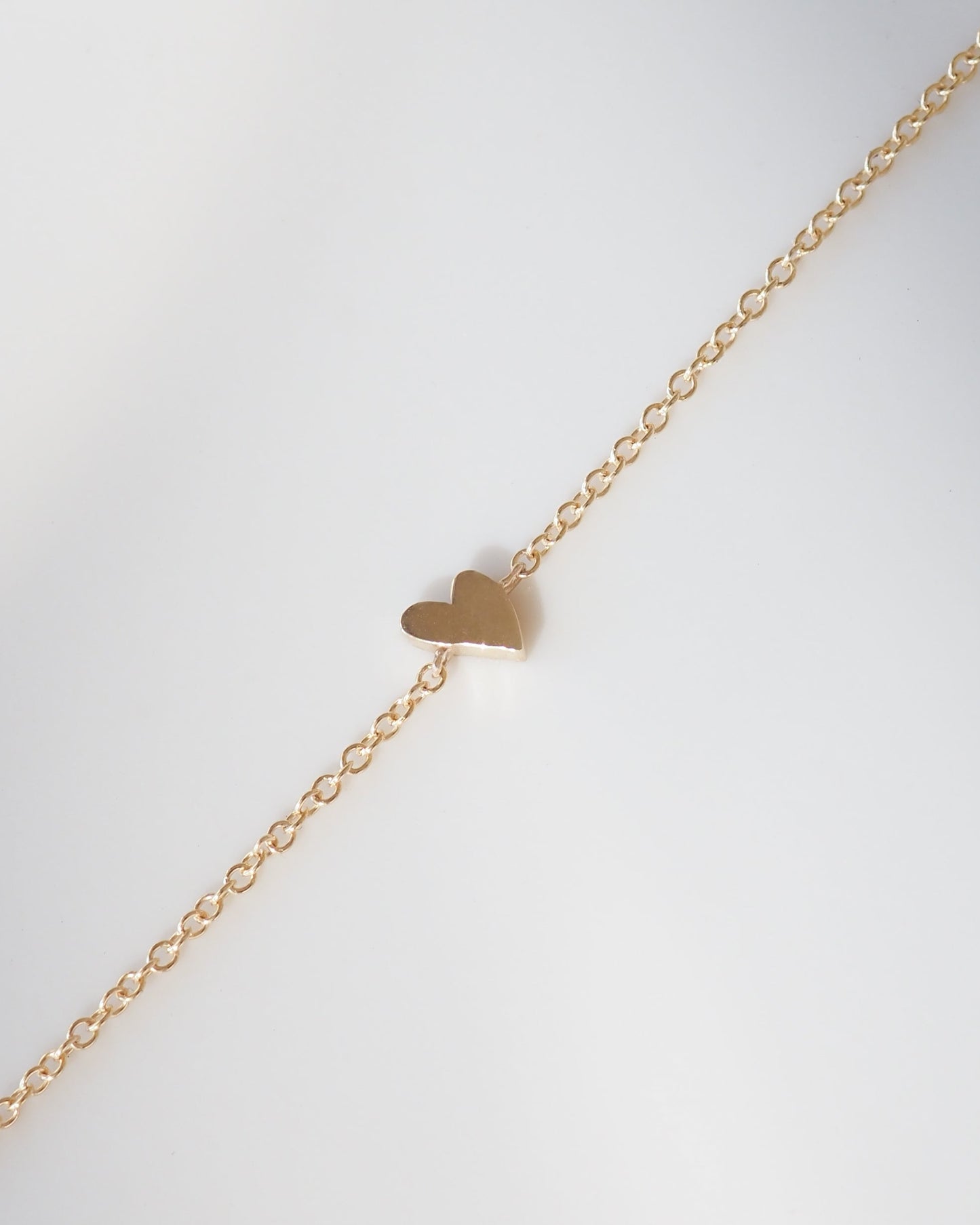 Gold heart-shaped pendant on a gold chain against a light gray background