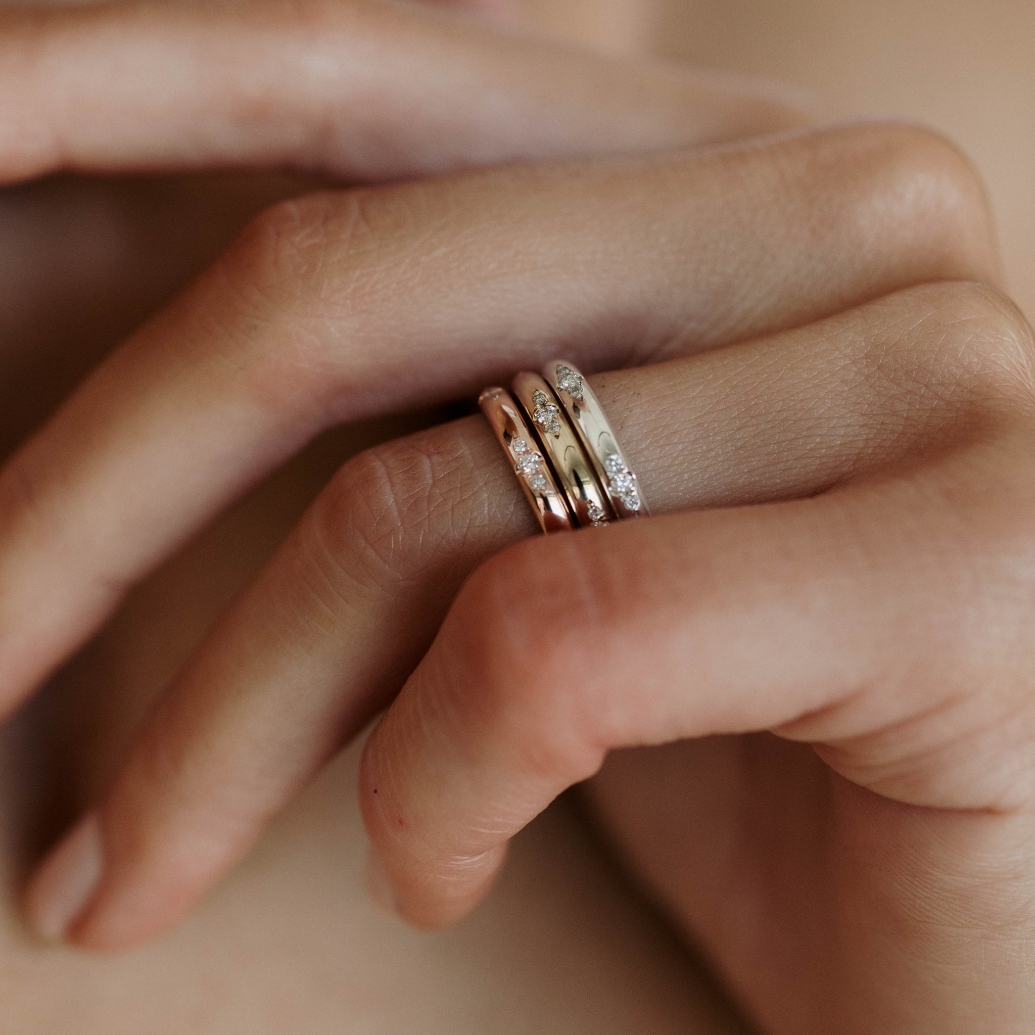 Close-up of a hand wearing three stacked diamond-encrusted rings in gold, rose gold, and white gold, showcasing luxury jewellery design.