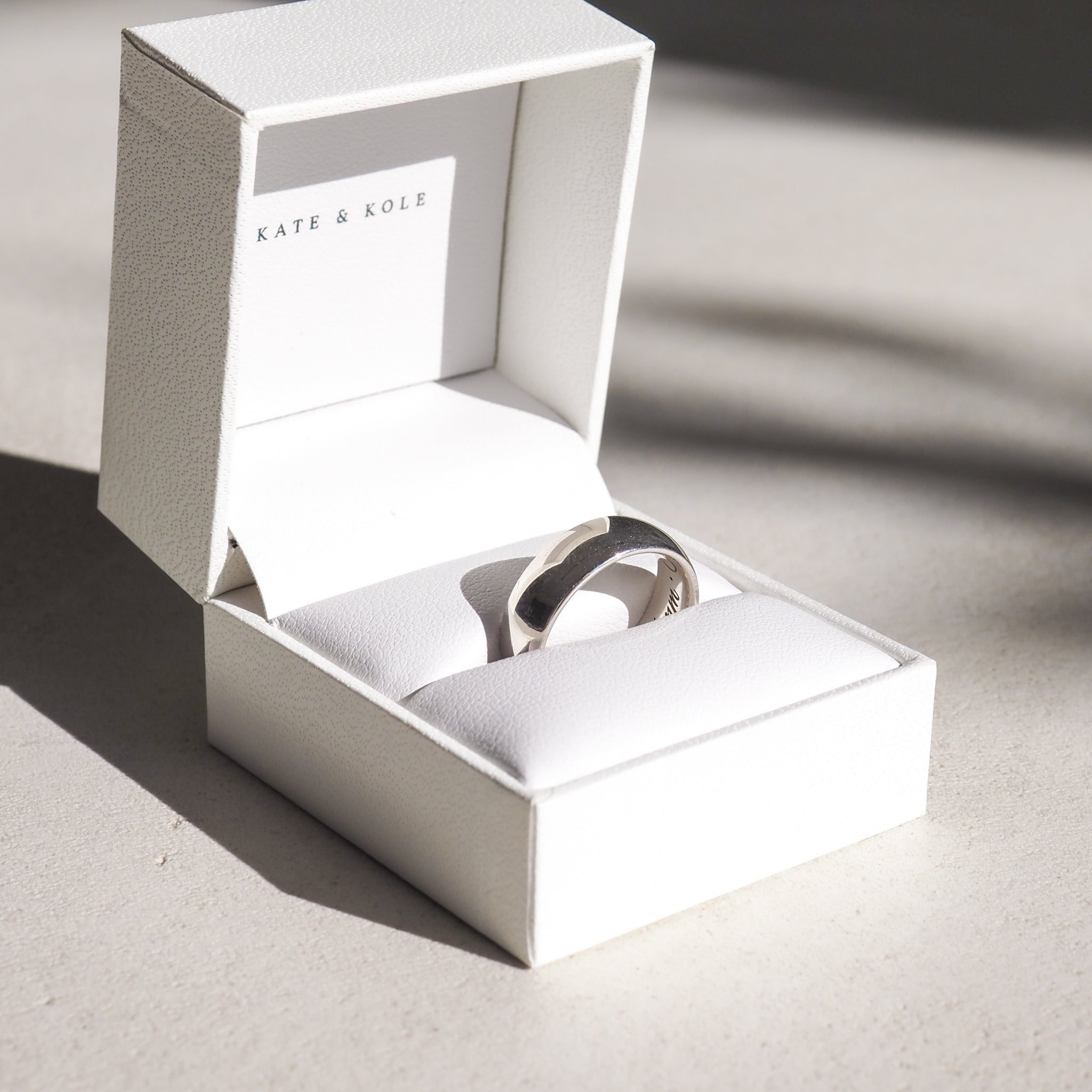 Silver ring elegantly displayed in a white Kate & Kole jewellery box, casting soft shadows on a light surface.