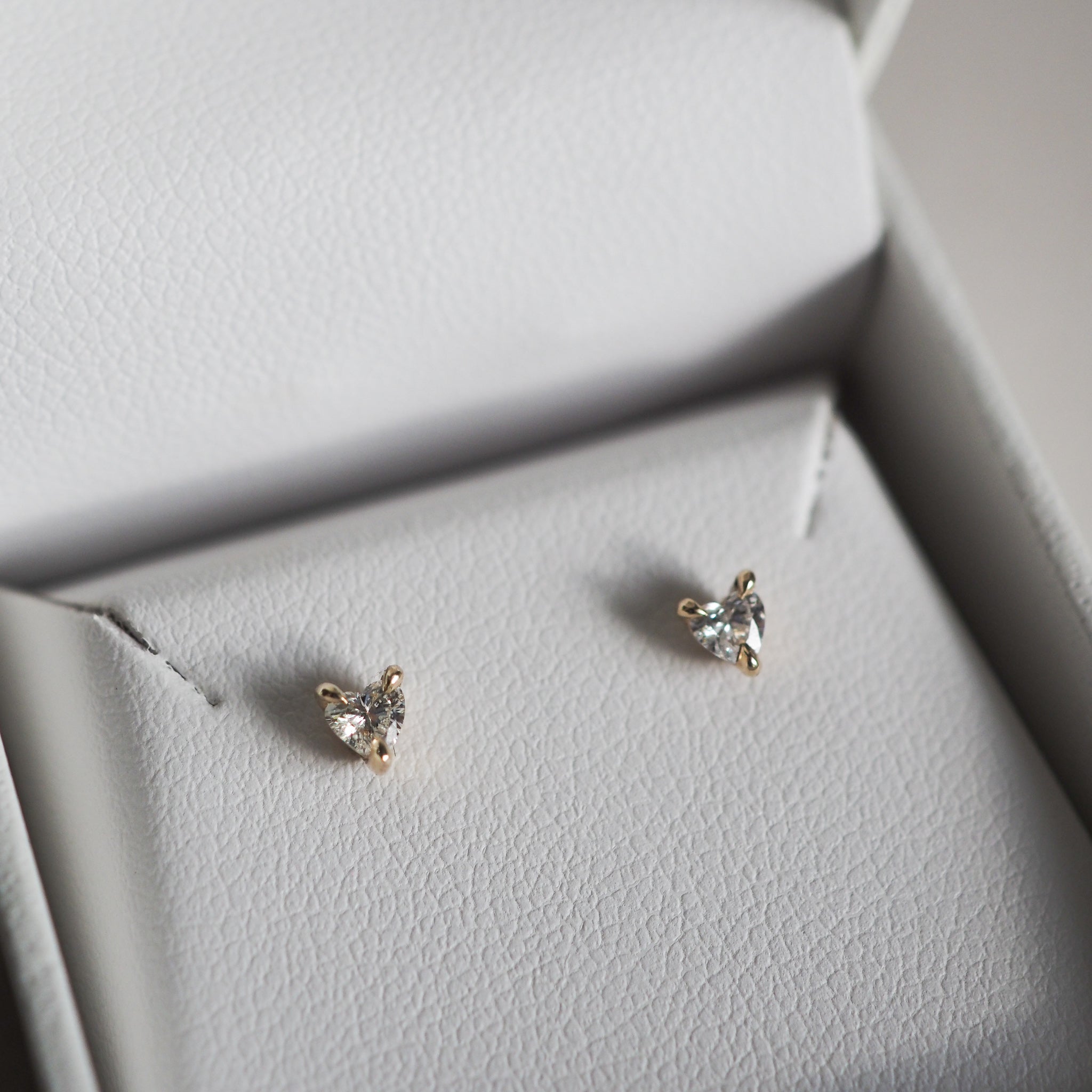 Gold and diamond stud earrings in a grey jewellery box, showcasing elegant triangular diamonds with a simple, luxurious design.