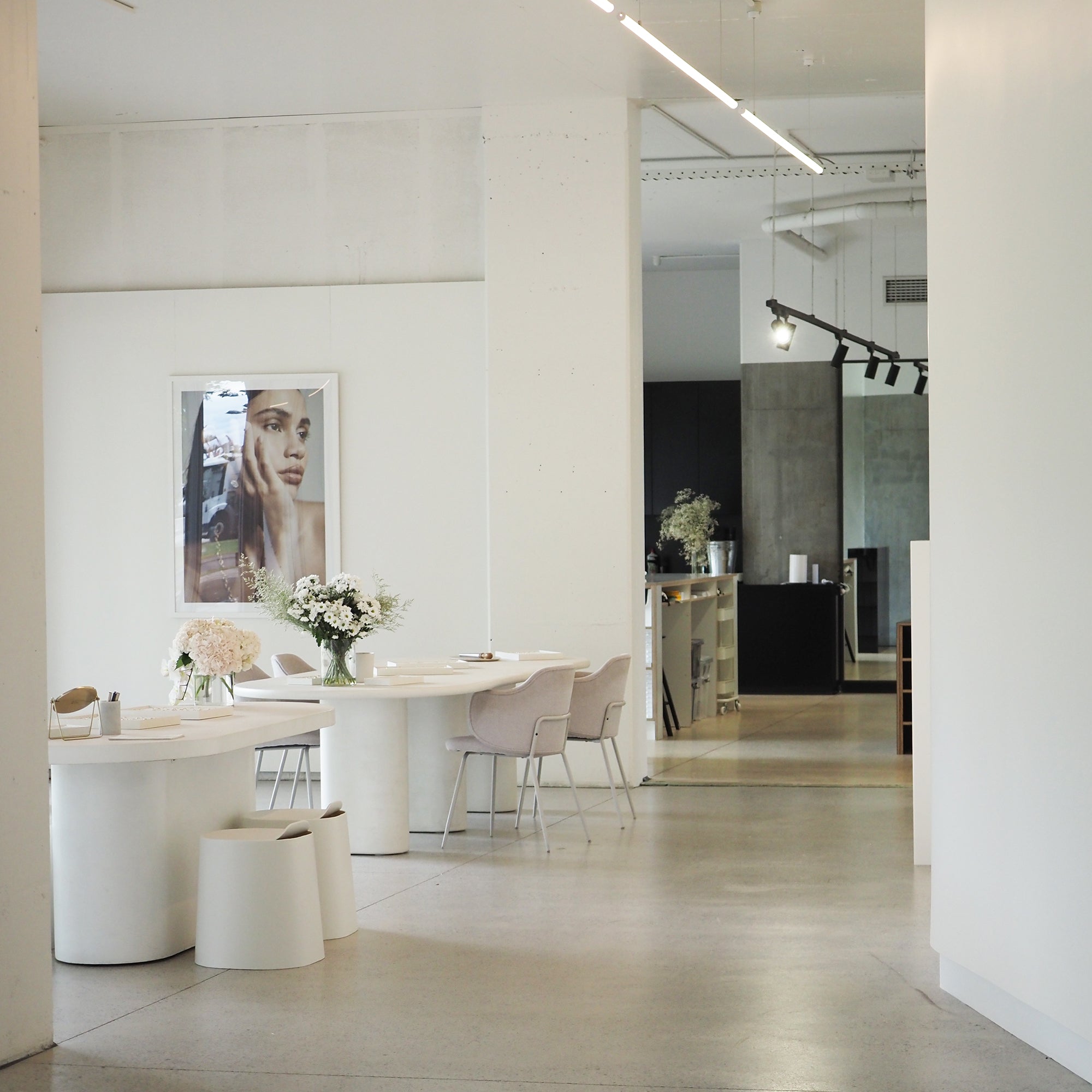 Minimalist jewellery boutique interior with elegant white decor, round tables, floral arrangements, and a fashion poster on the wall.