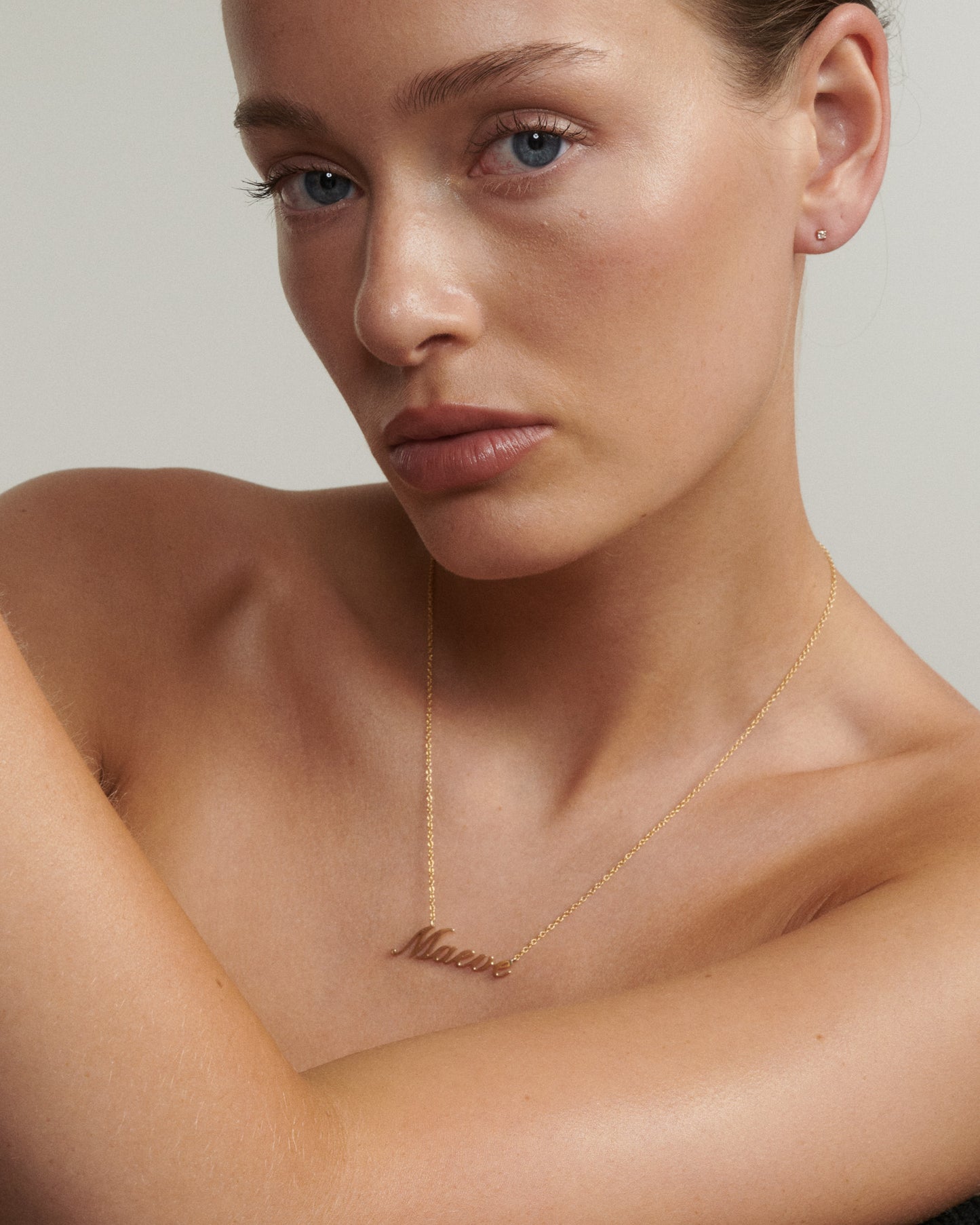 Woman wearing a gold necklace with 'Melrose' pendant against a neutral background