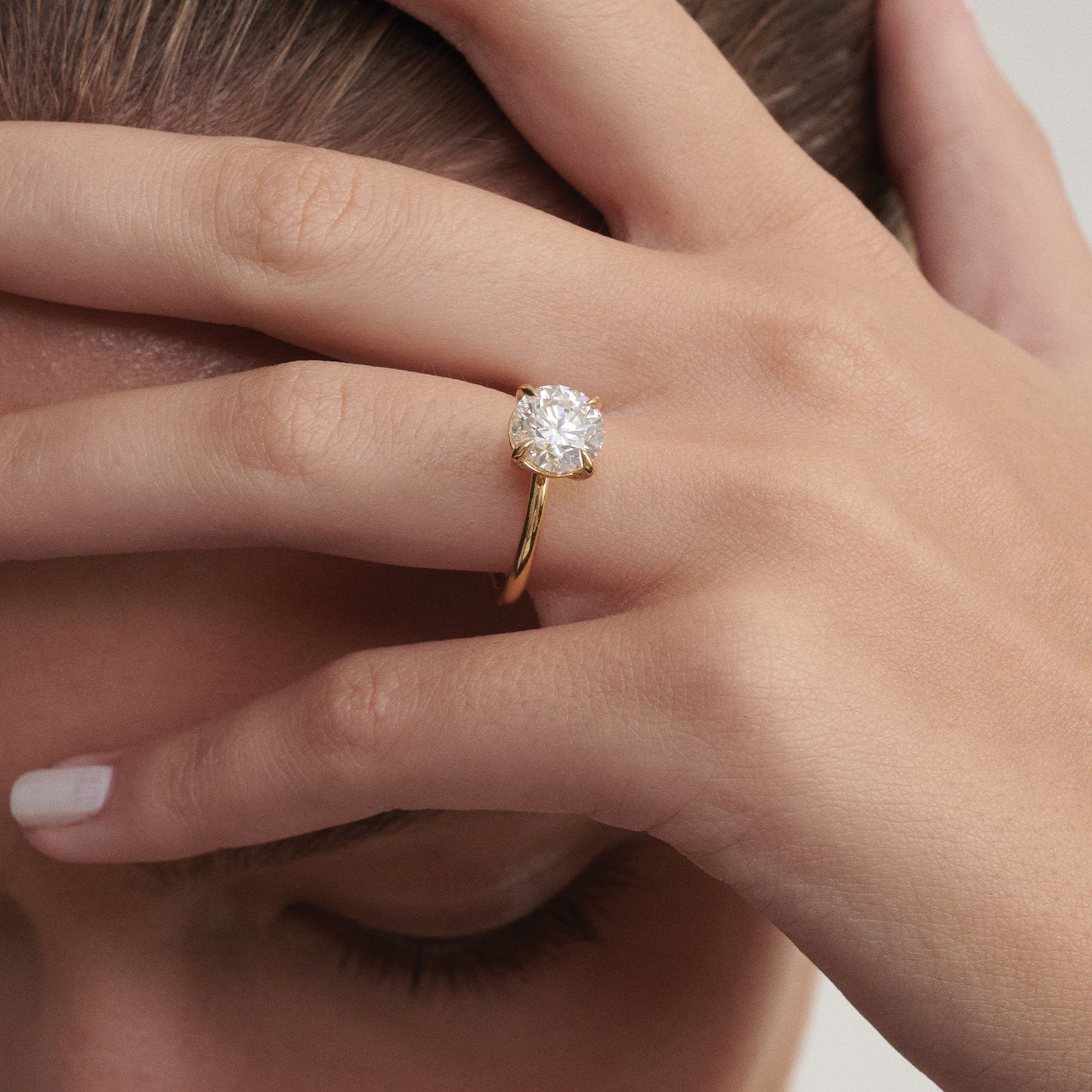 Close-up of a hand wearing a gold ring with a diamond, holding hair.
