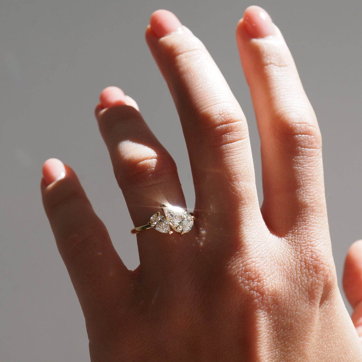 Hand model wearing a duet pear diamond ring with a neutral background