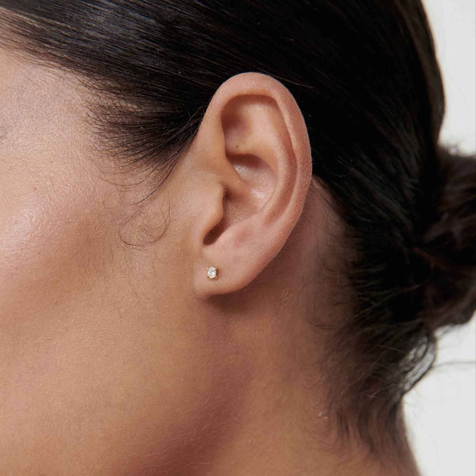 Close-up of woman’s ear wearing a small diamond stud earring; smooth complexion, minimalist high-end jewellery style.