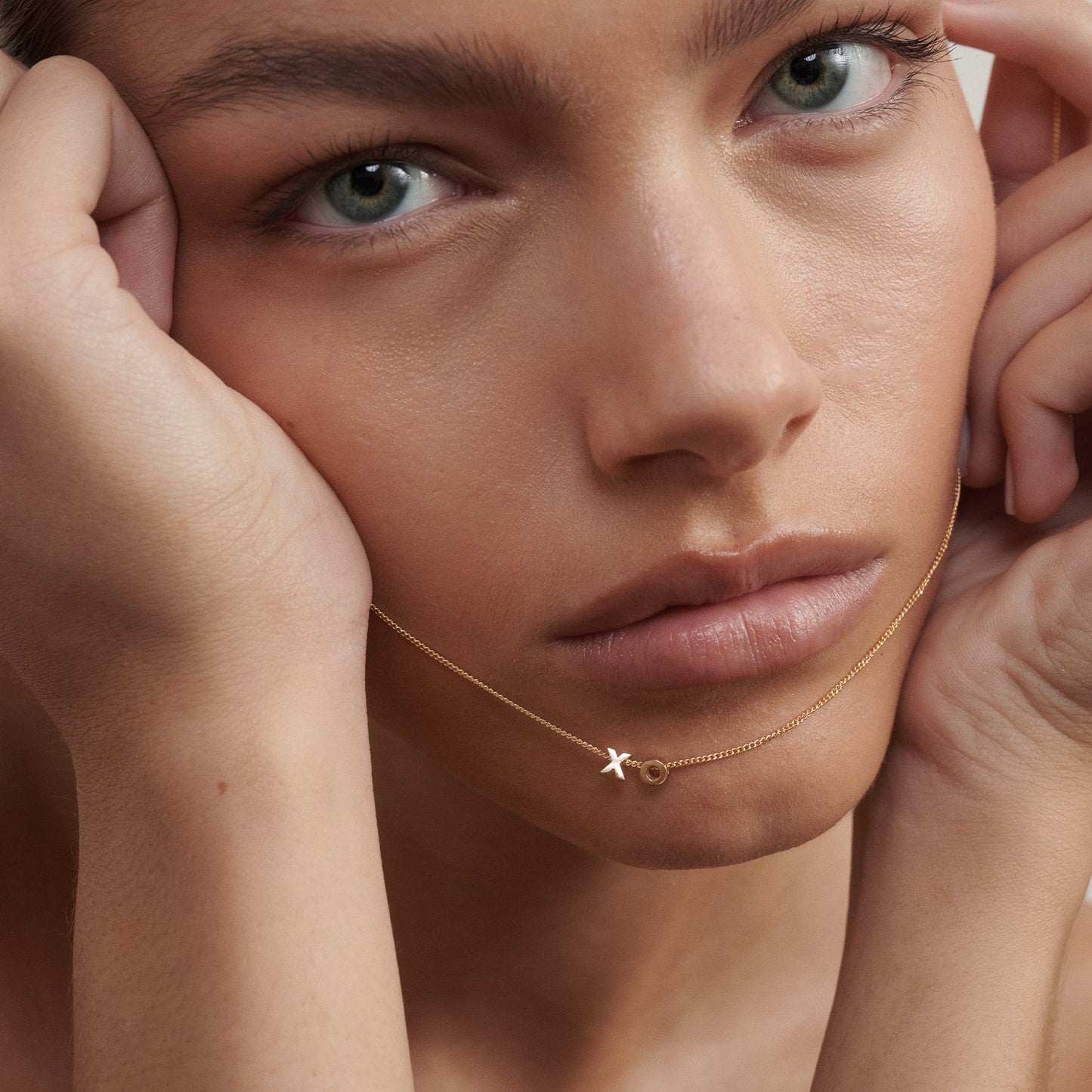 Close-up of a woman's face wearing a gold necklace with a X and O pendant.

[text overlay: Worn with two sliding charms]