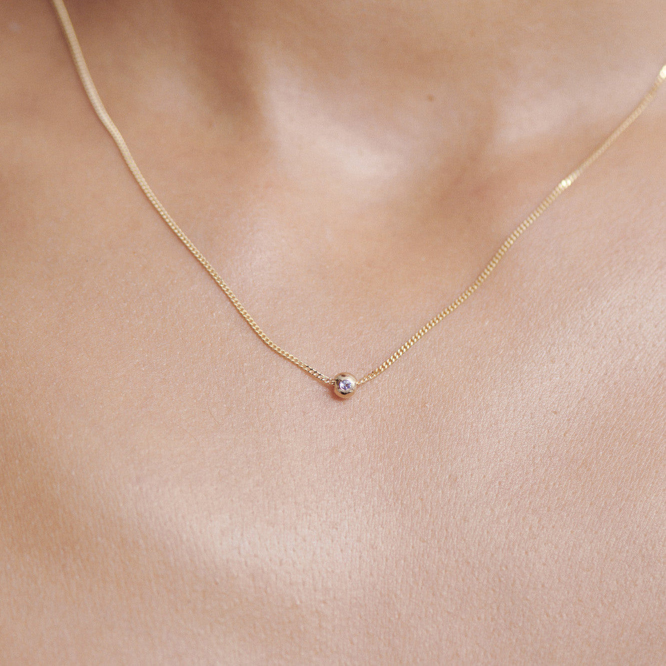 Gold necklace with a small round amethyst pendant on a person's neck