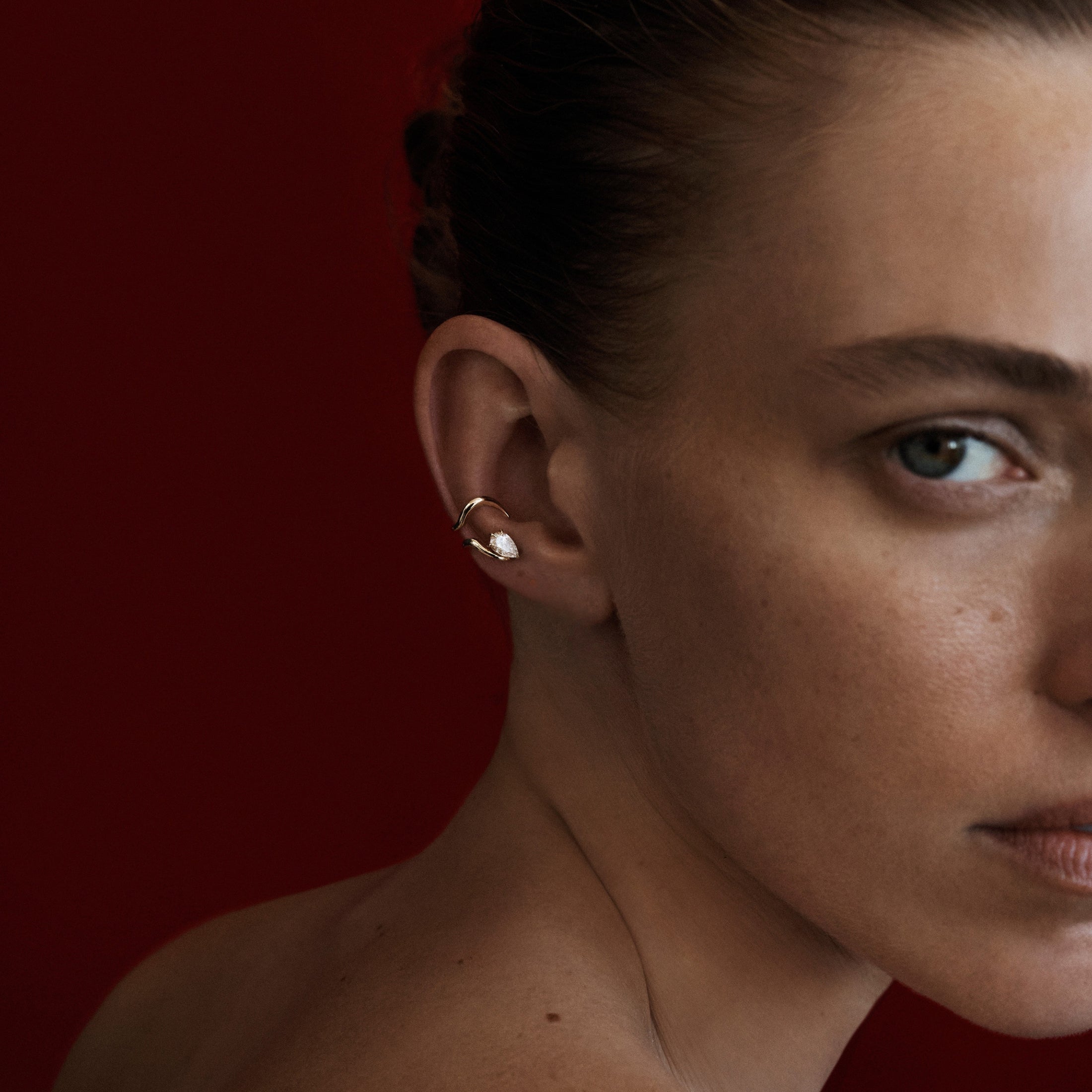 Close-up of a woman's ear with an earring against a red background