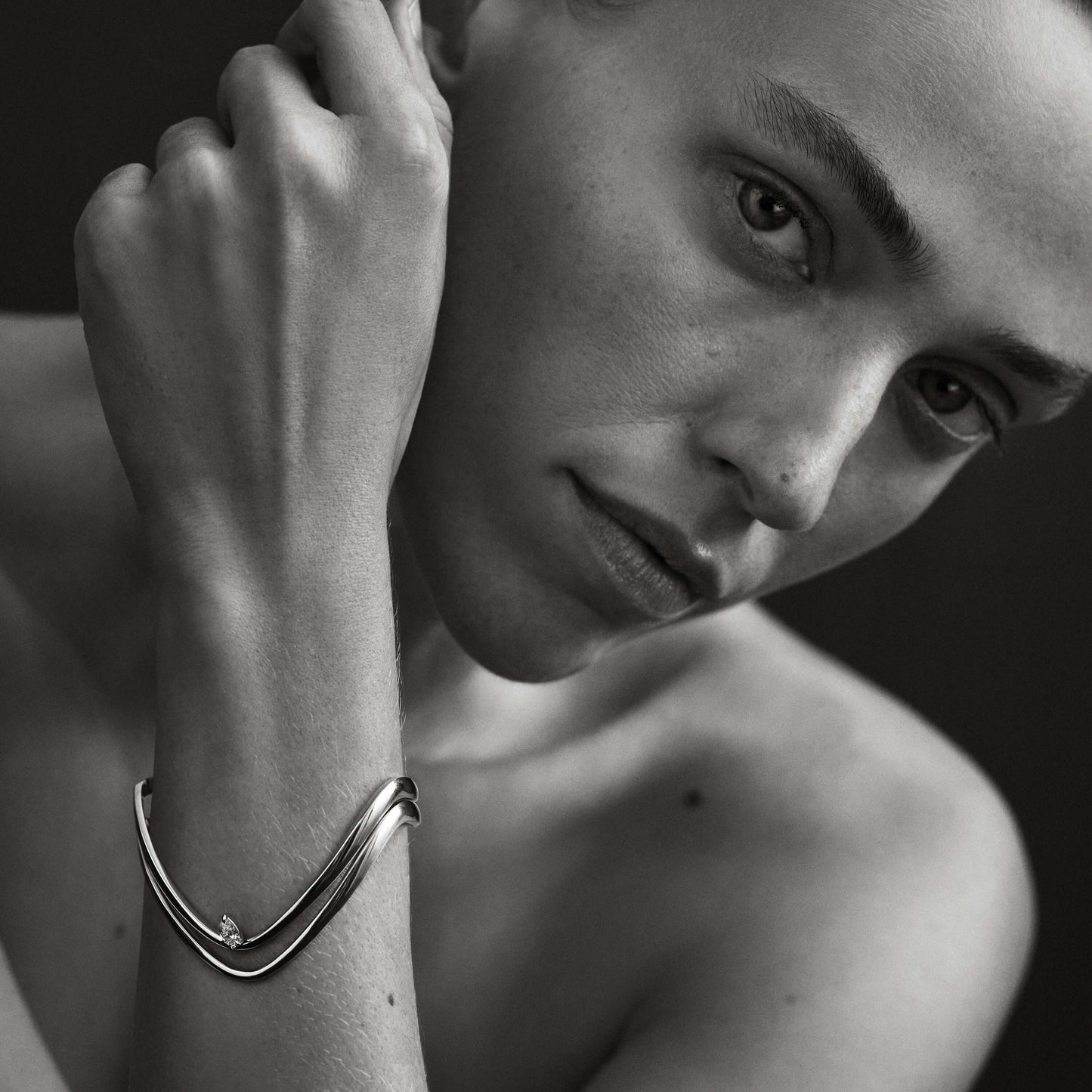 Black and white close-up of a person wearing a bracelet.
[text overlay: Model wears Piece 5—The Forme Bangle above Piece 8—The Sol Bangle]
