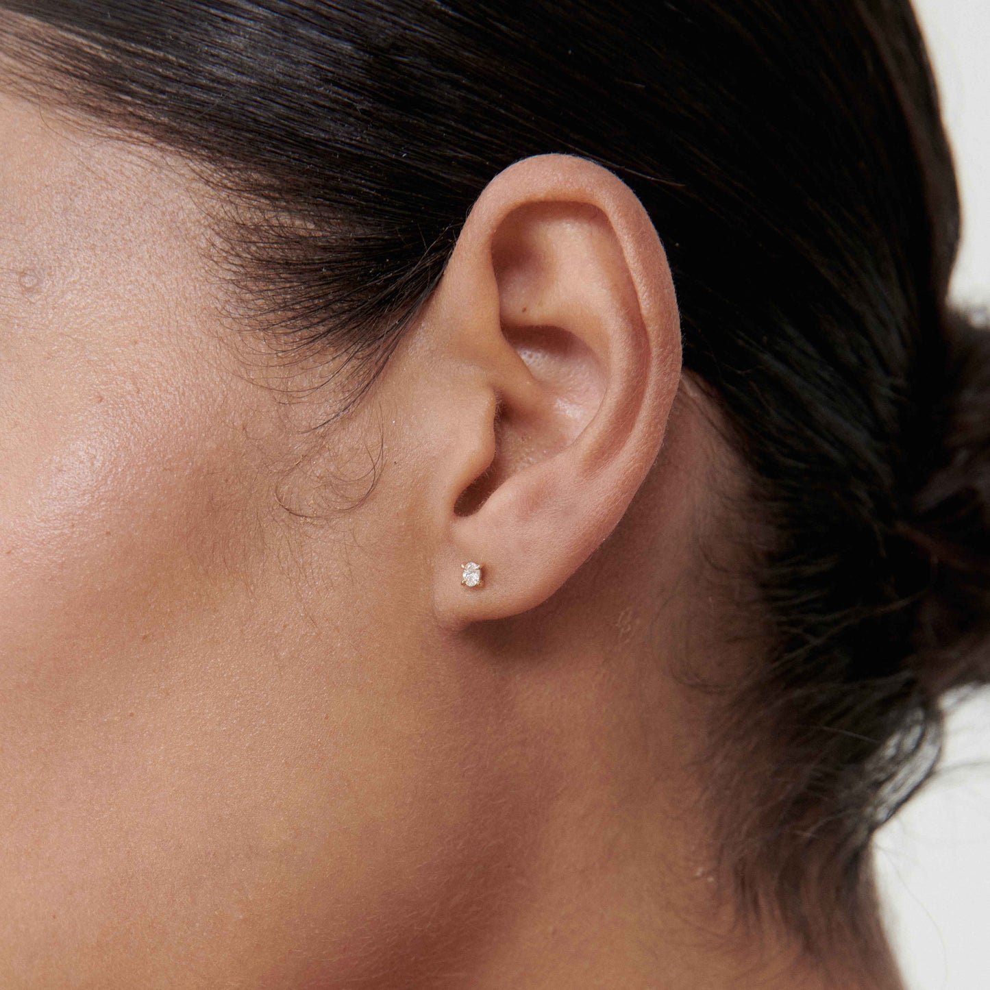 Close-up of a woman's ear wearing a small diamond stud earring, showcasing luxury jewellery. Minimalist and elegant design.
[text overlay: Oval Diamond Studs][text colour: #000000]