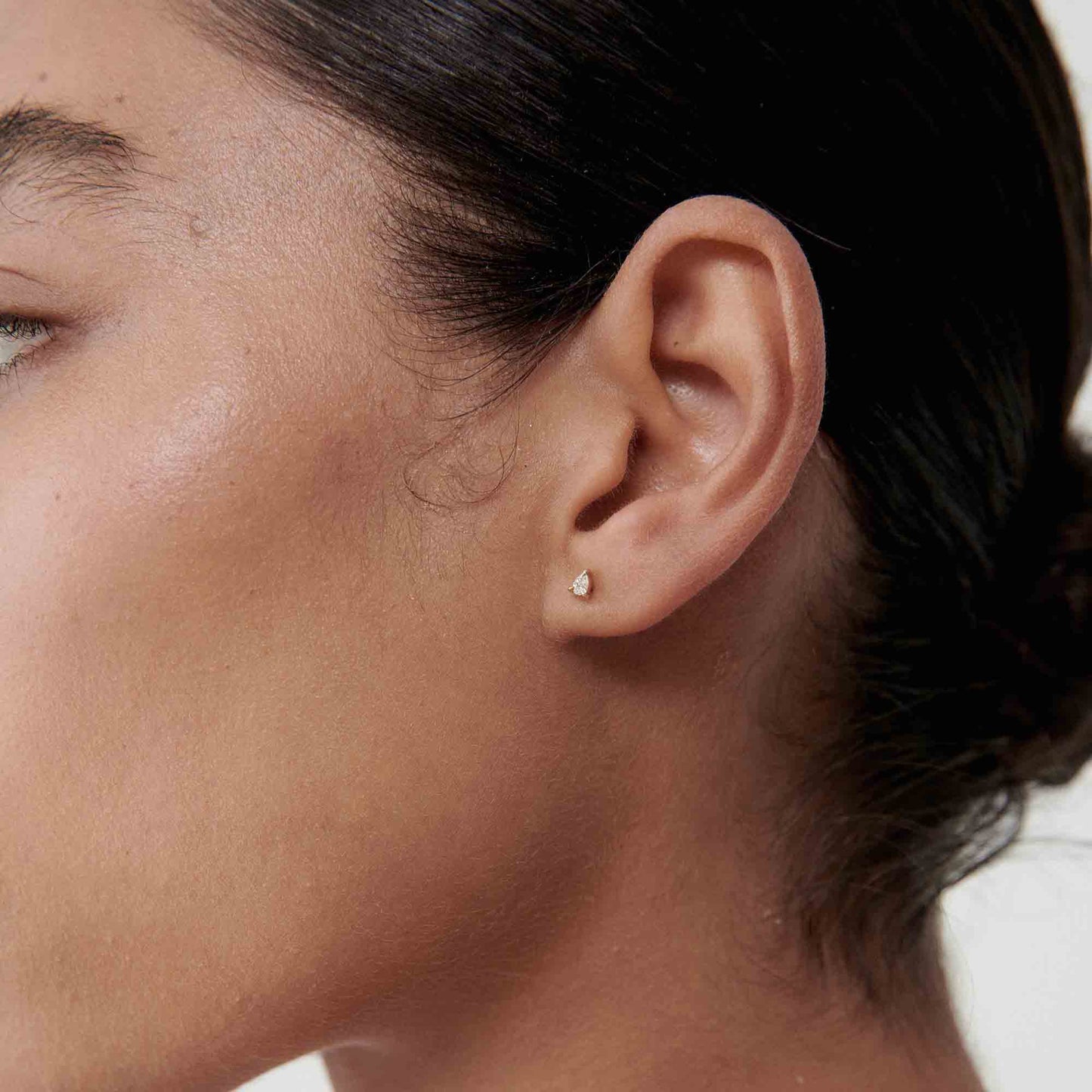 Profile of a person wearing a small, elegant diamond stud earring, showcasing minimalist luxury jewellery.[text overlay: Pear Diamond Studs][text colour: #000000]