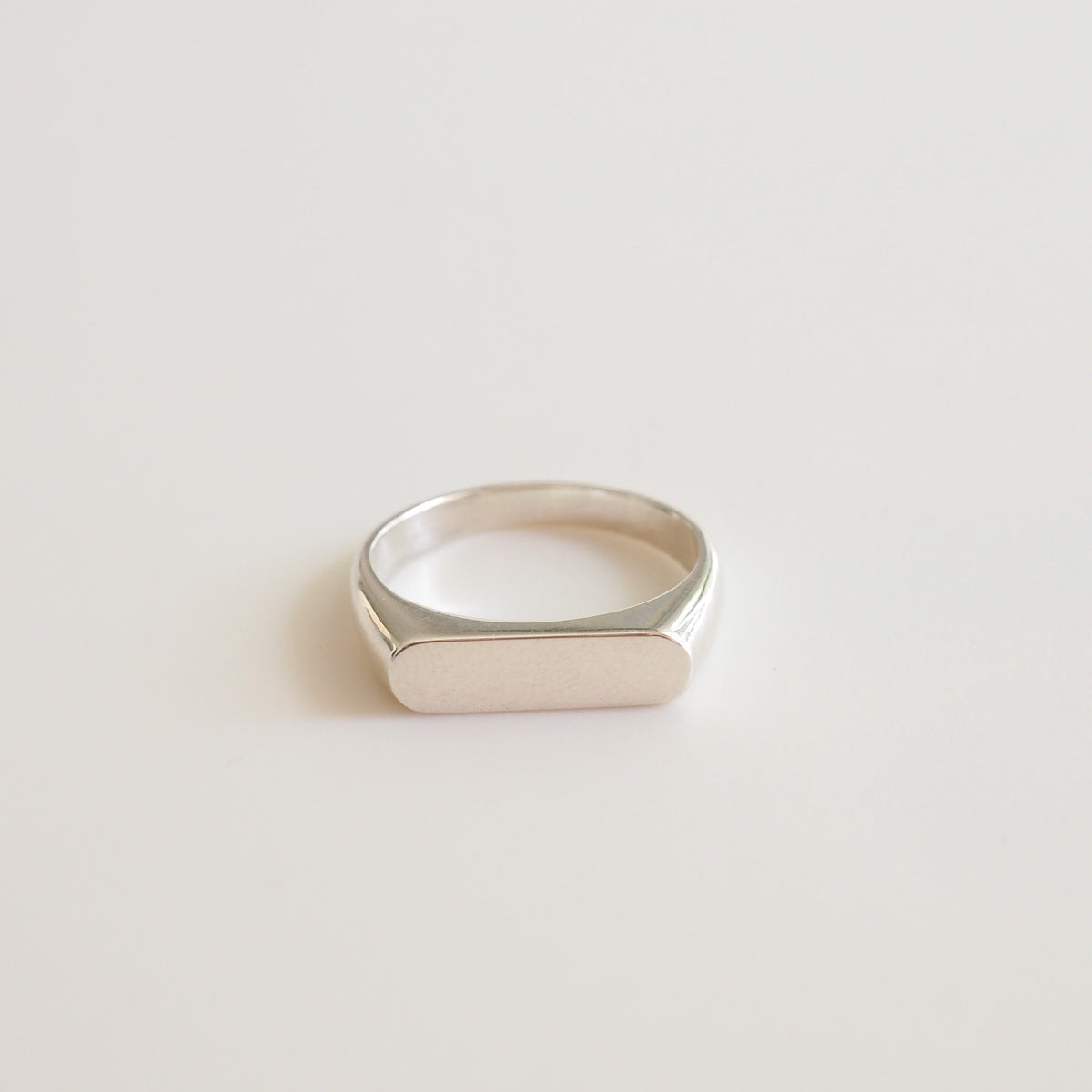 A flaylay of a narrow silver signet ring on a white background