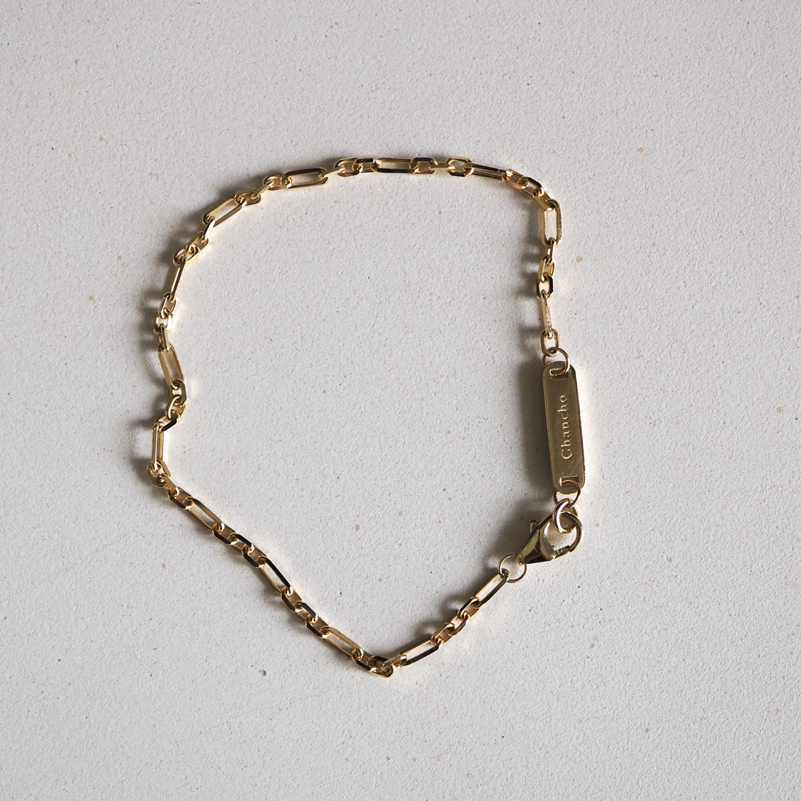 Gold link bracelet with an engraved rectangular pendant on a light grey background. Luxury jewellery, elegant design.