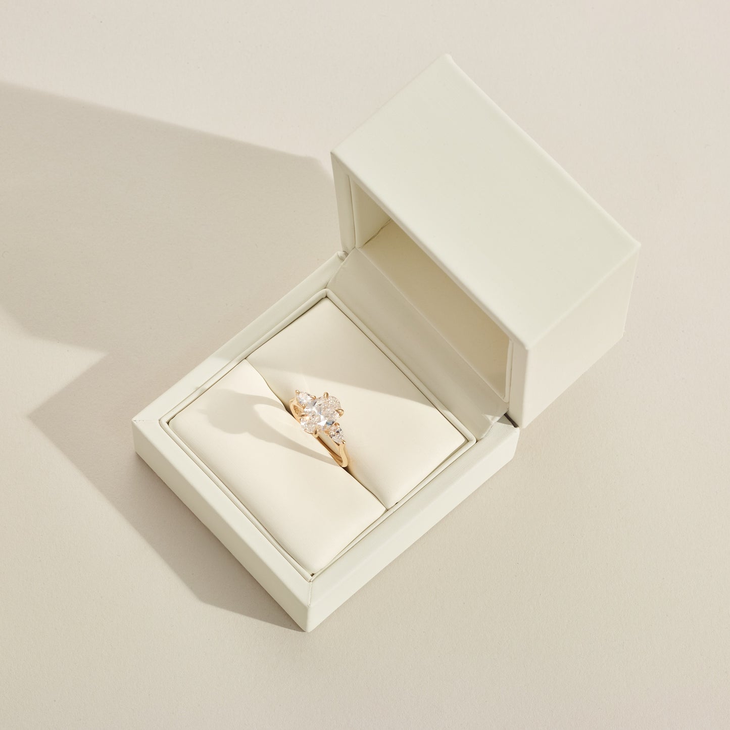 Gold ring in a box with a 3 diamonds on a light beige background