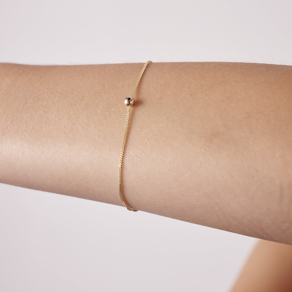 Minimalist gold chain bracelet with a single bead on a person's wrist, showcasing luxury jewellery.[text overlay: Ruby stone set]