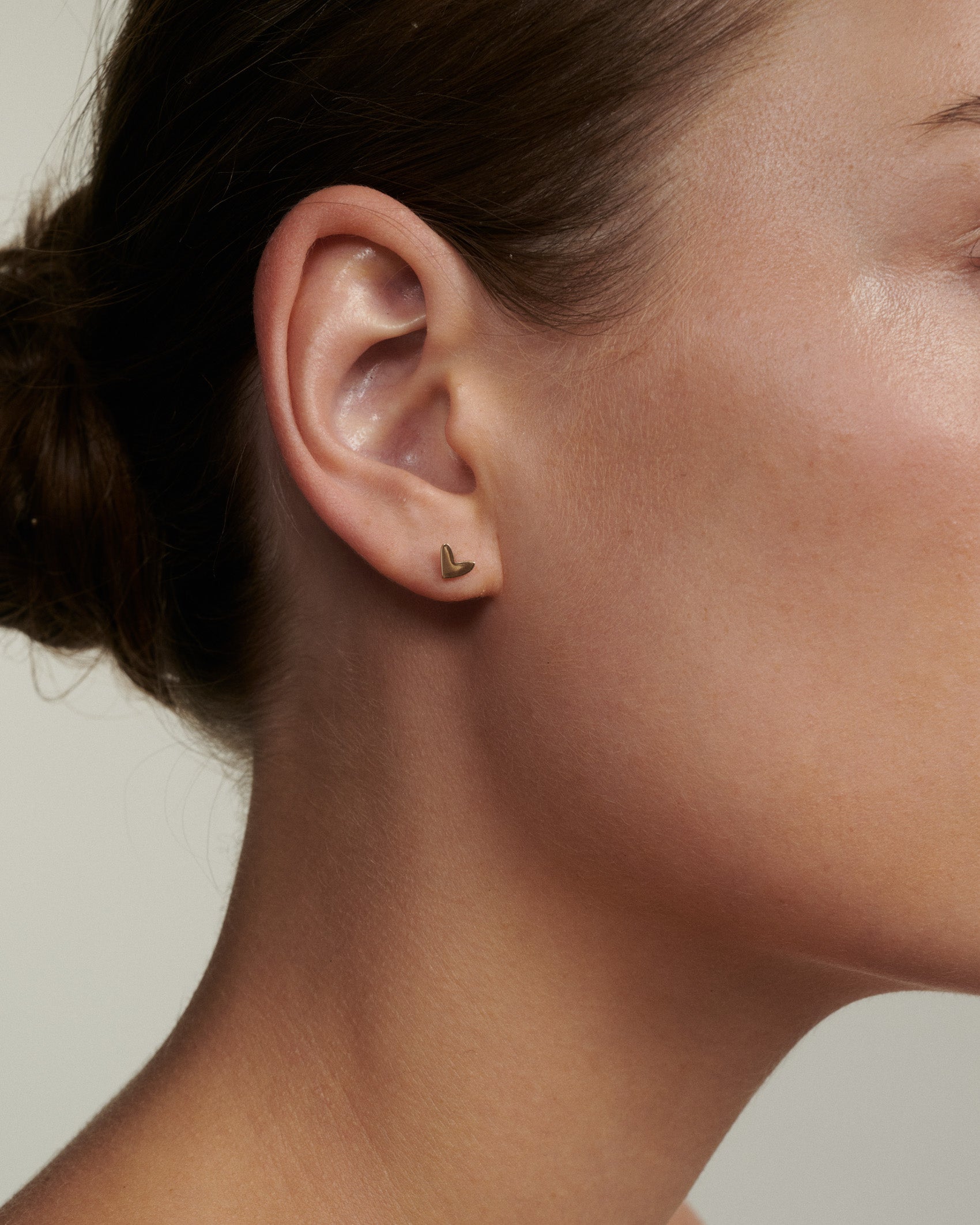 Close-up of an ear wearing a small earring with a neutral background