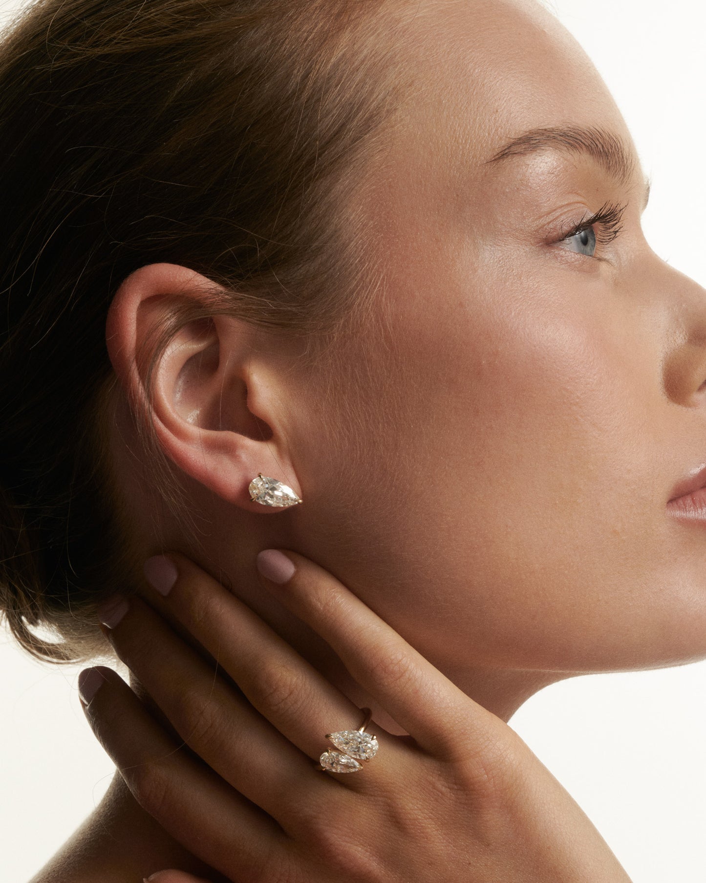 Close-up of a woman wearing diamond earrings and a ring on a neutral background