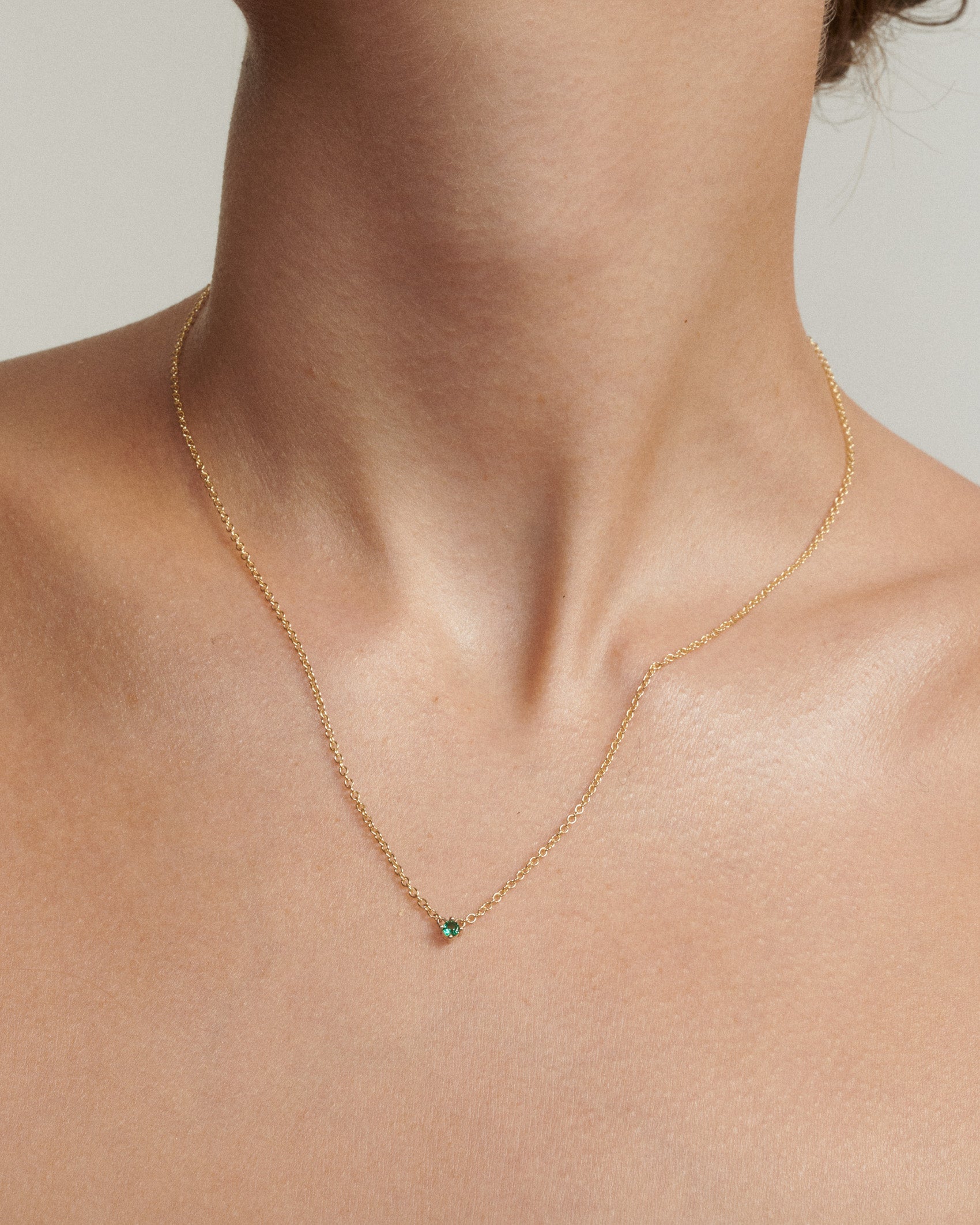 Gold necklace with a green gemstone on a person's neck against a neutral background