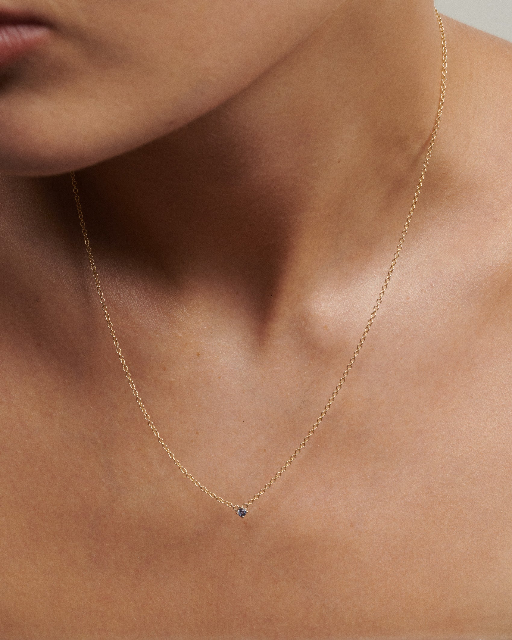 Gold necklace with a small blue gemstone on a person's neck