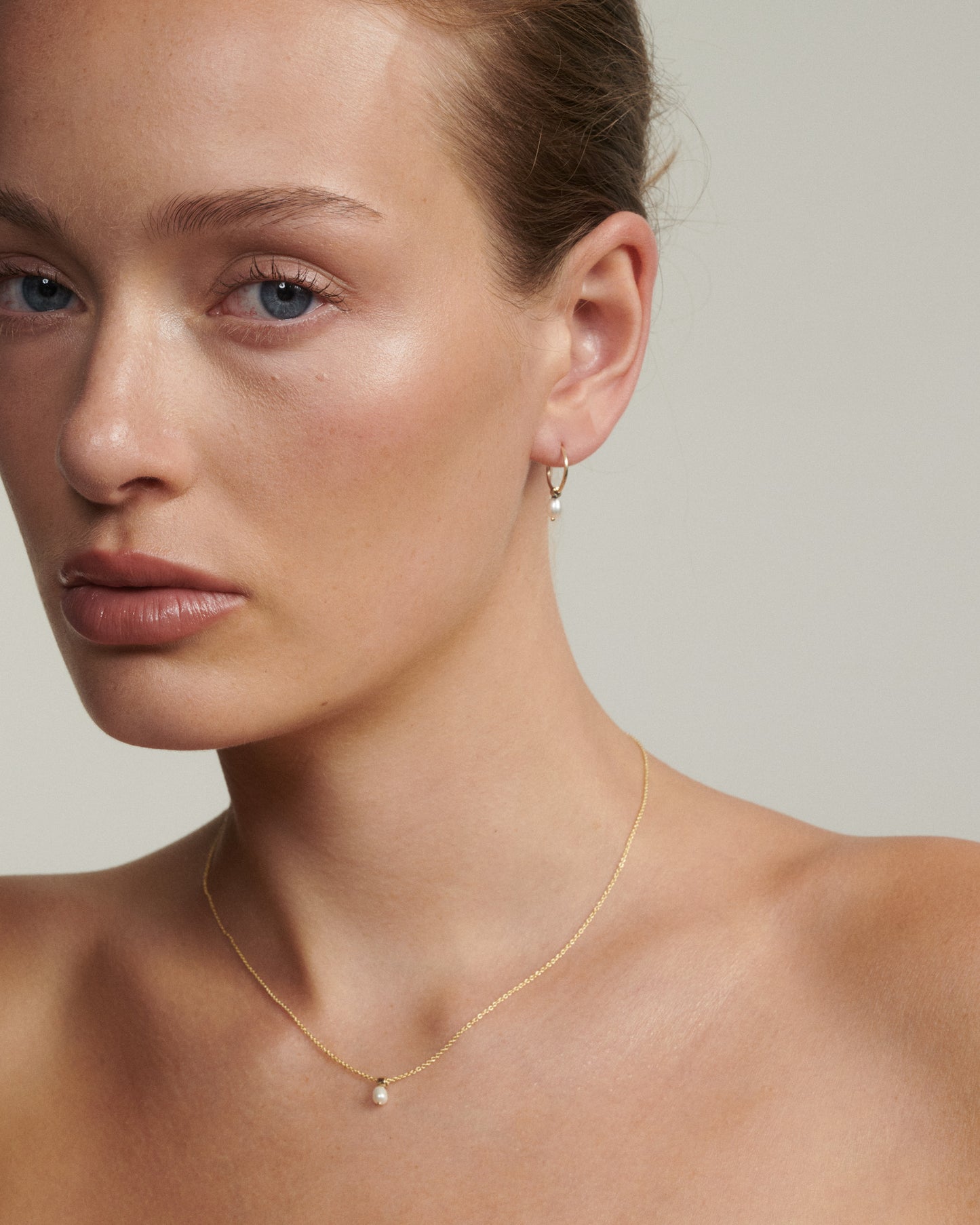 Woman wearing a gold necklace and earring on a neutral background