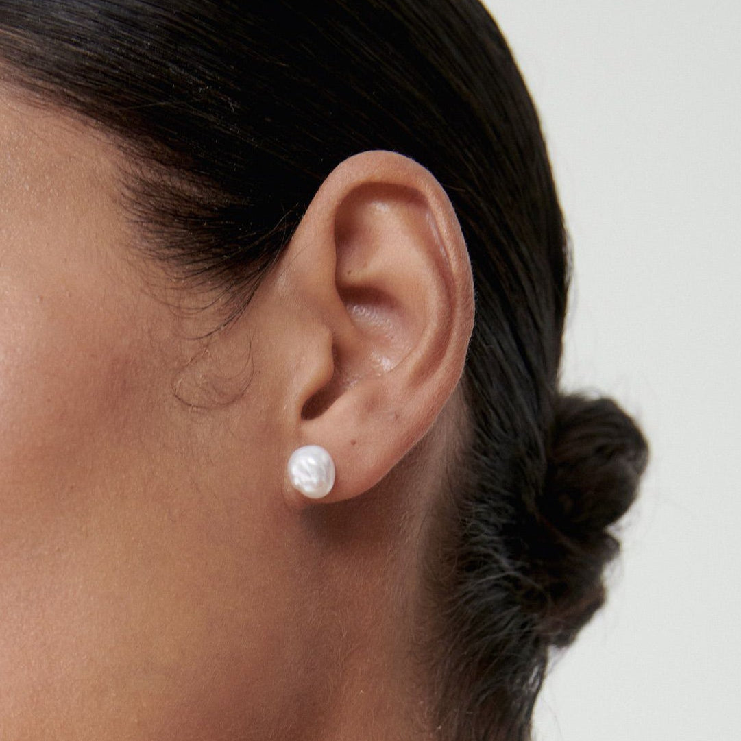 Profile of a woman wearing an elegant pearl stud earring, showcasing minimalist luxury jewellery with a sleek hairstyle against a soft background.