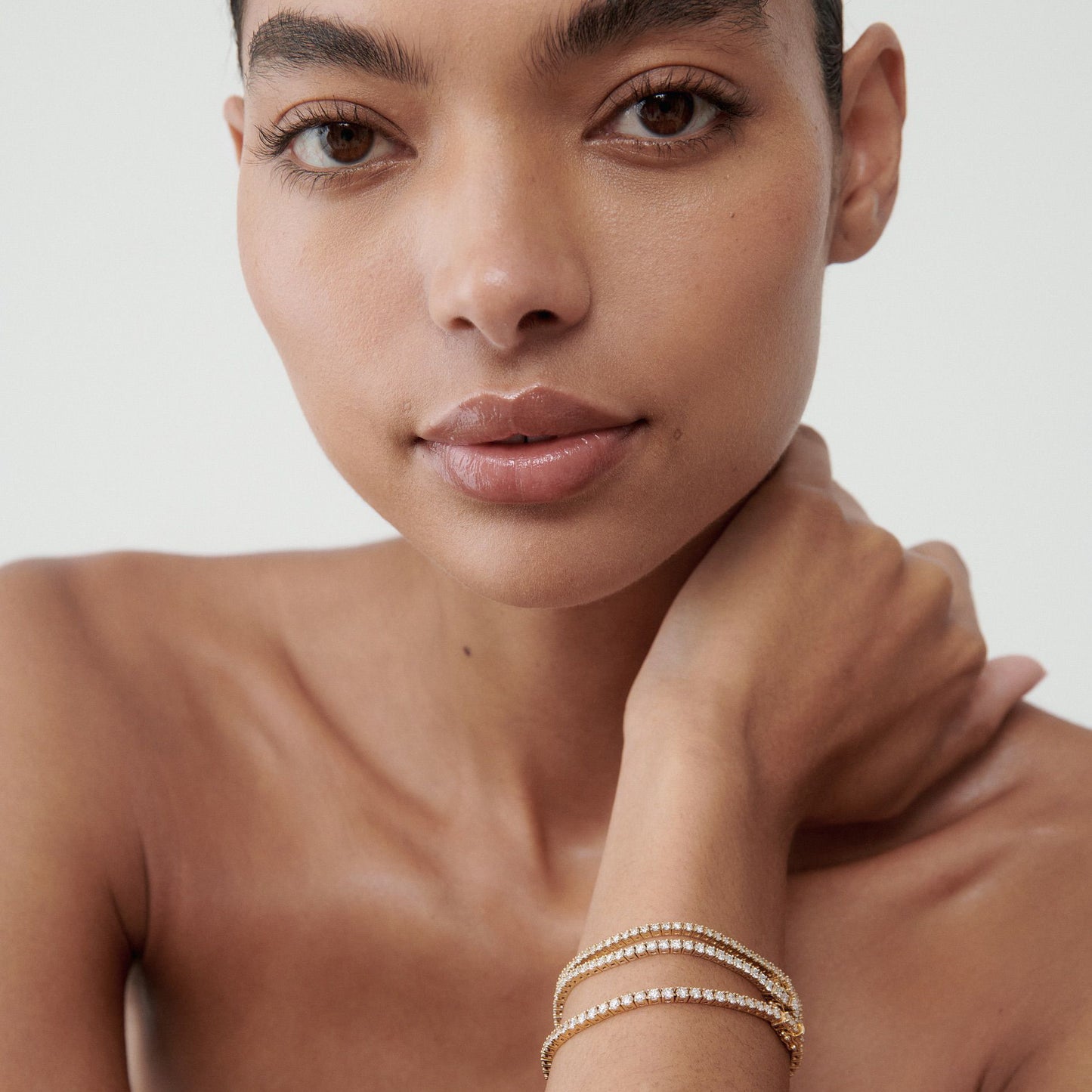 Woman with elegant diamond bracelets on wrist, showcasing luxury jewellery against a neutral background..