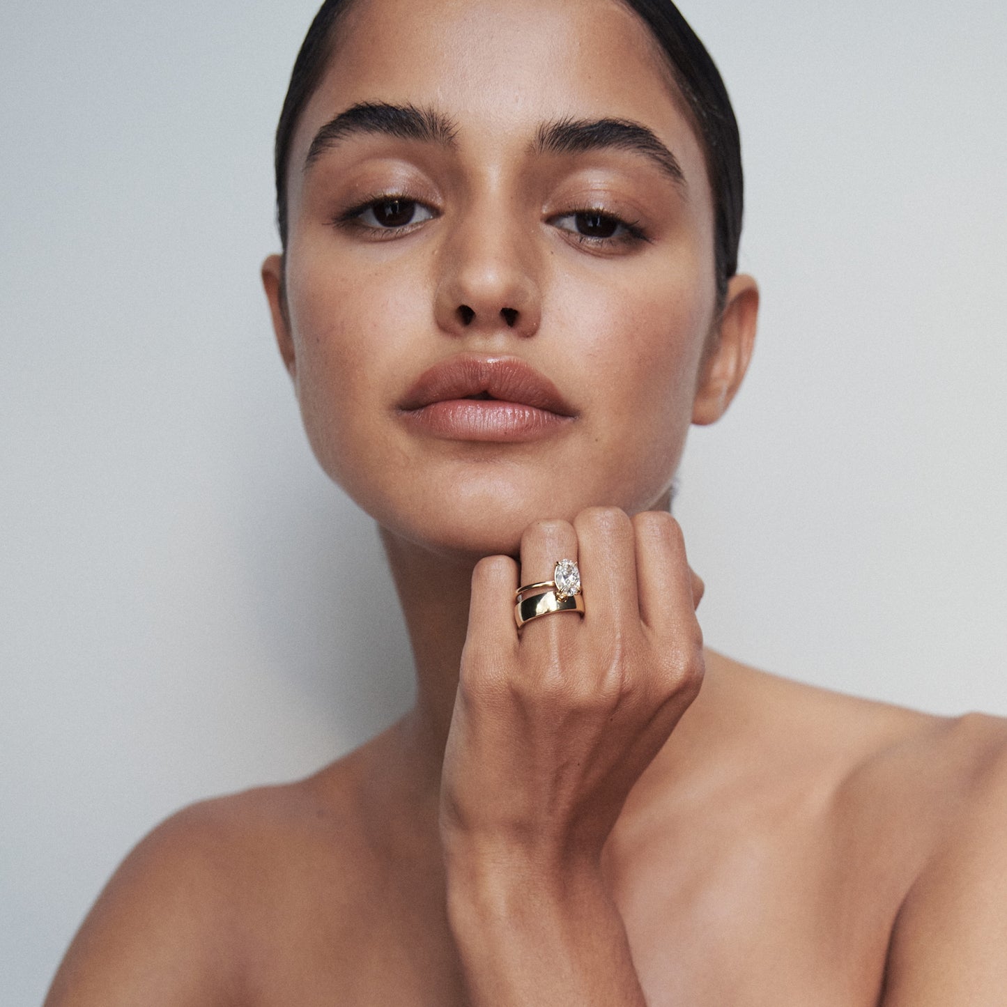 Woman showcasing a luxurious gold ring with a prominent diamond, highlighting high-end jewellery. Neutral background enhances elegance.