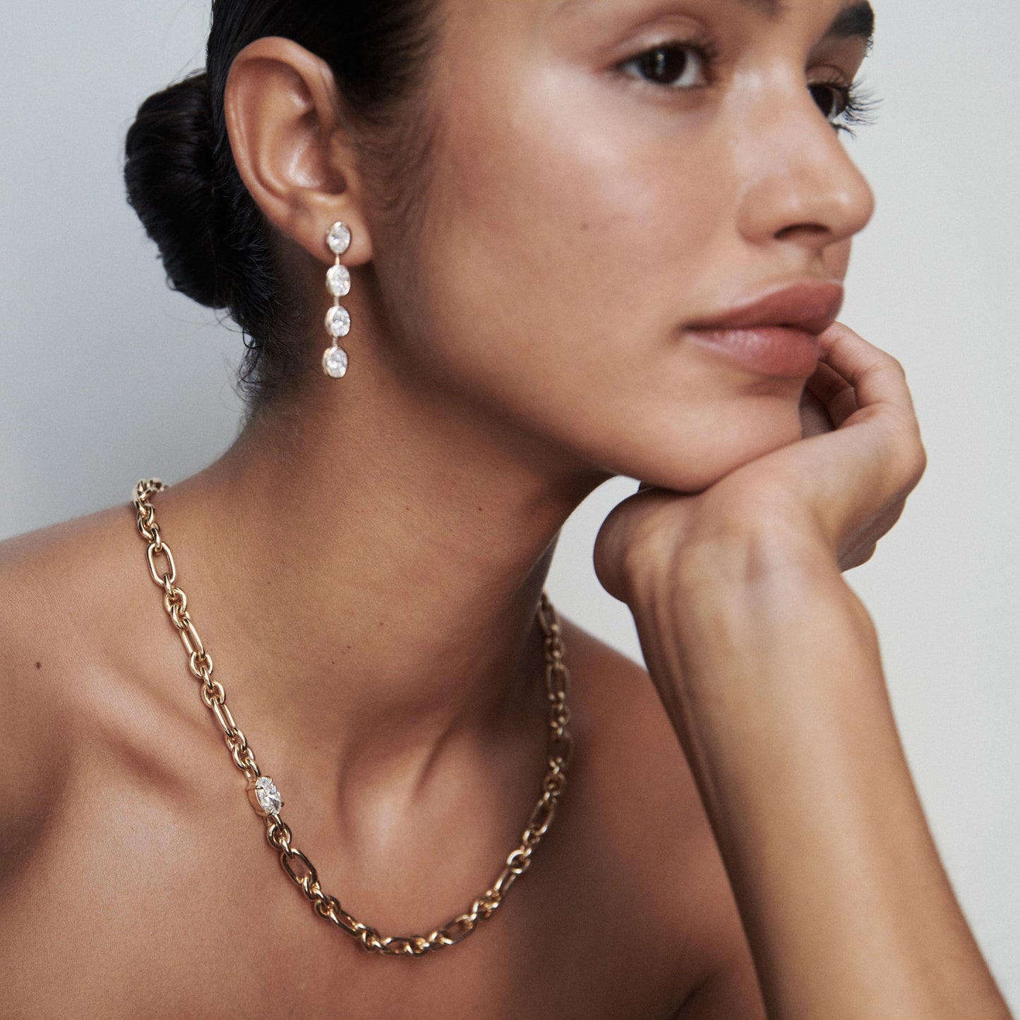 Woman wearing luxury gold chain necklace and drop earrings featuring sparkling gems, captured in a minimalist style.