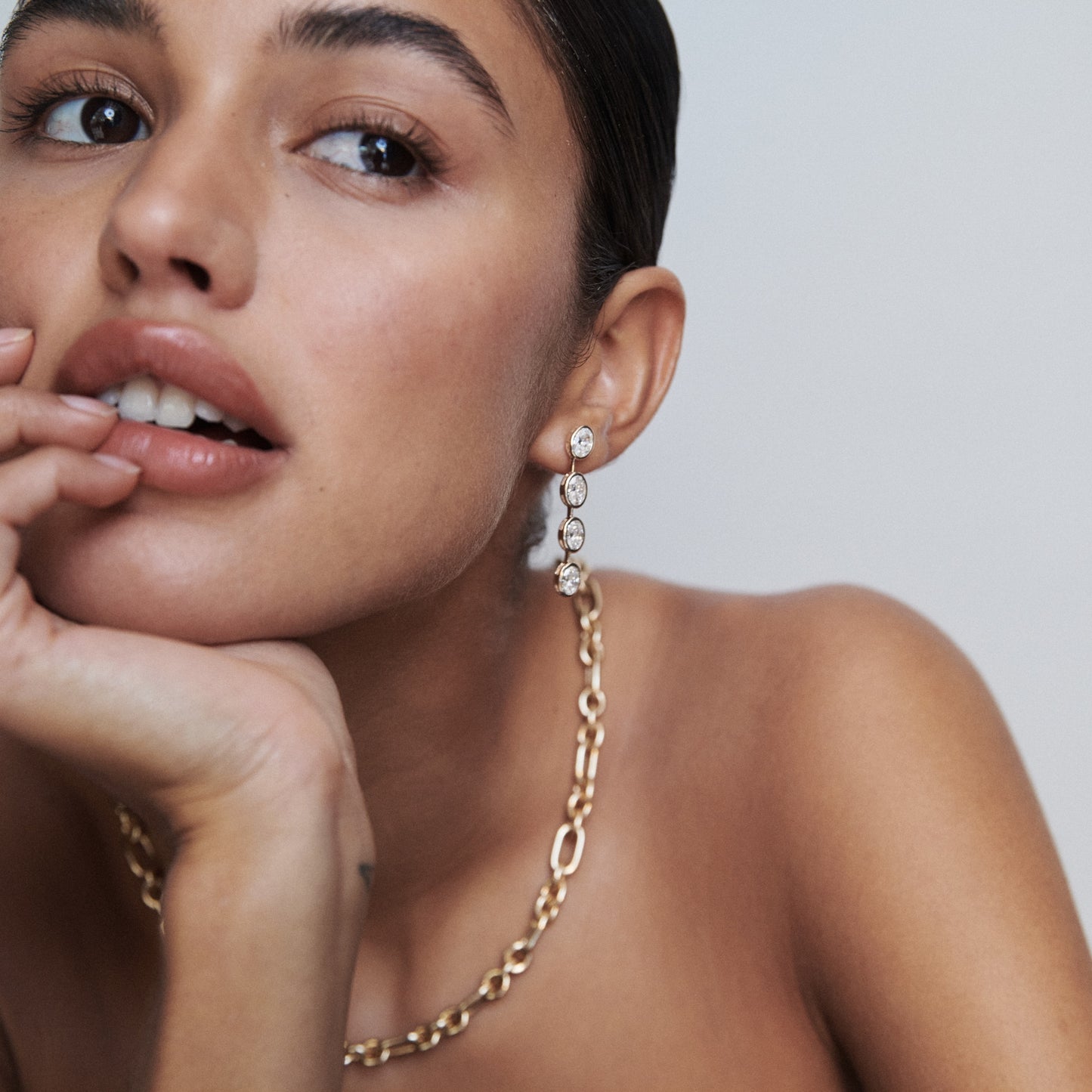Woman wearing elegant diamond drop earrings and a chunky gold chain necklace, gazing to the side. Luxe jewellery, minimalist style.