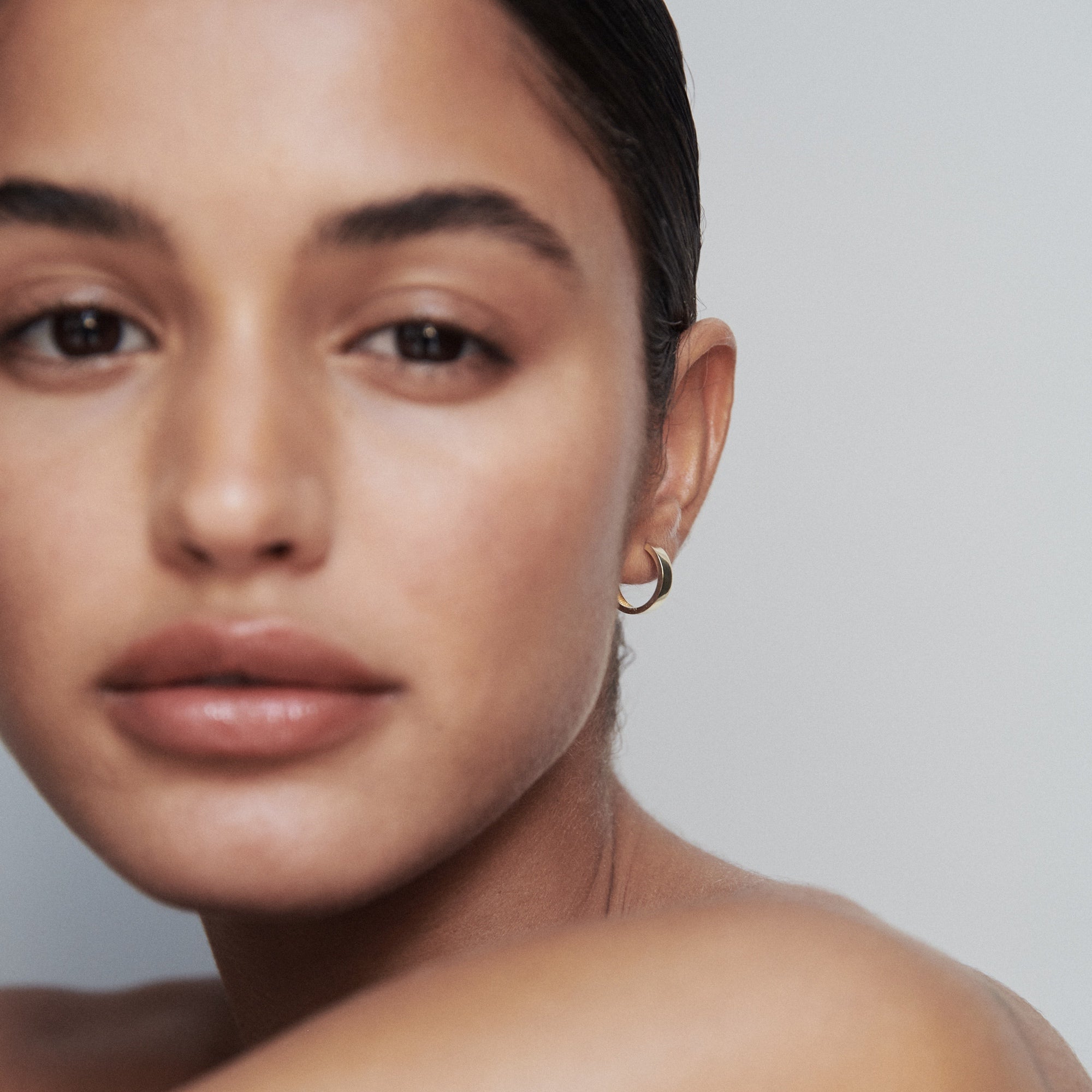 Close-up of a woman's face wearing a gold hoop earring, with clear skin and minimalist makeup, exuding luxury and elegance.