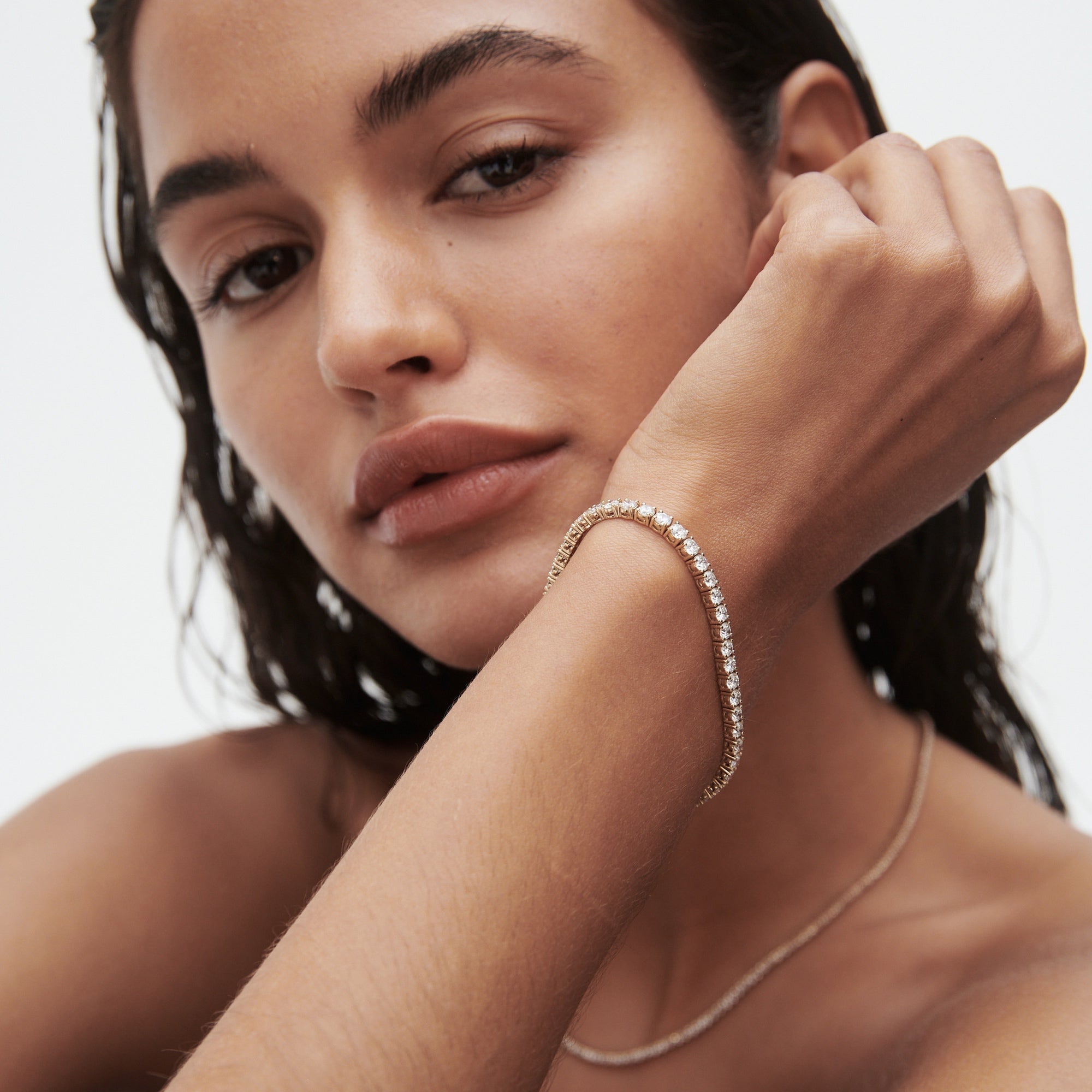 Woman wearing an elegant diamond tennis bracelet, showcasing luxury jewellery. Natural makeup and wet-look hair enhance the sophisticated style.[text overlay: ]