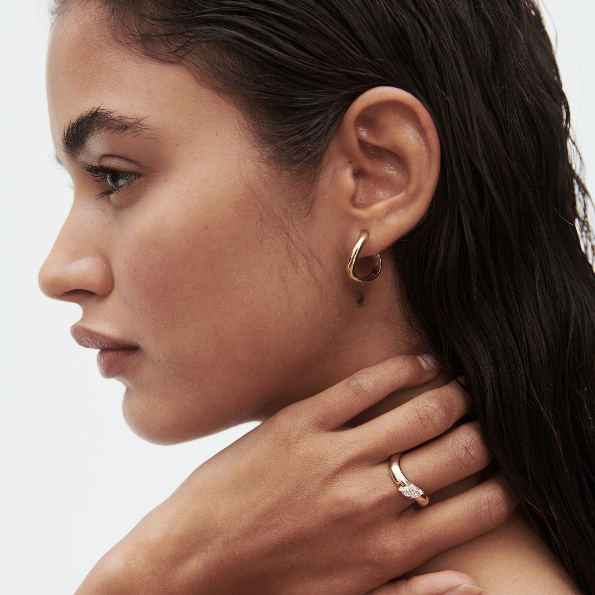 Woman with wet hair wearing gold hoop earrings and a diamond ring, looking pensive. Luxury jewellery, elegant style, close-up profile.