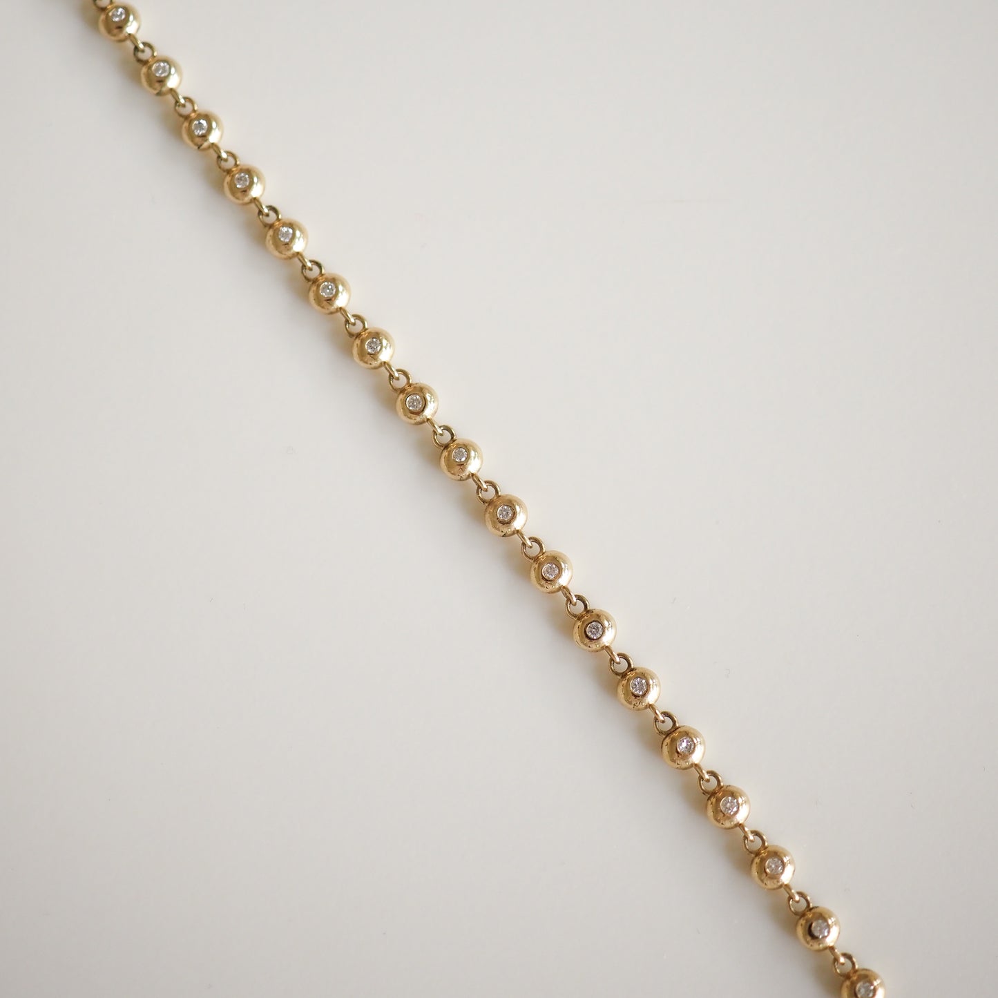 Gold chain bracelet with round diamond bezels, elegantly linked, set against a plain background. Perfect for luxury jewellery enthusiasts.