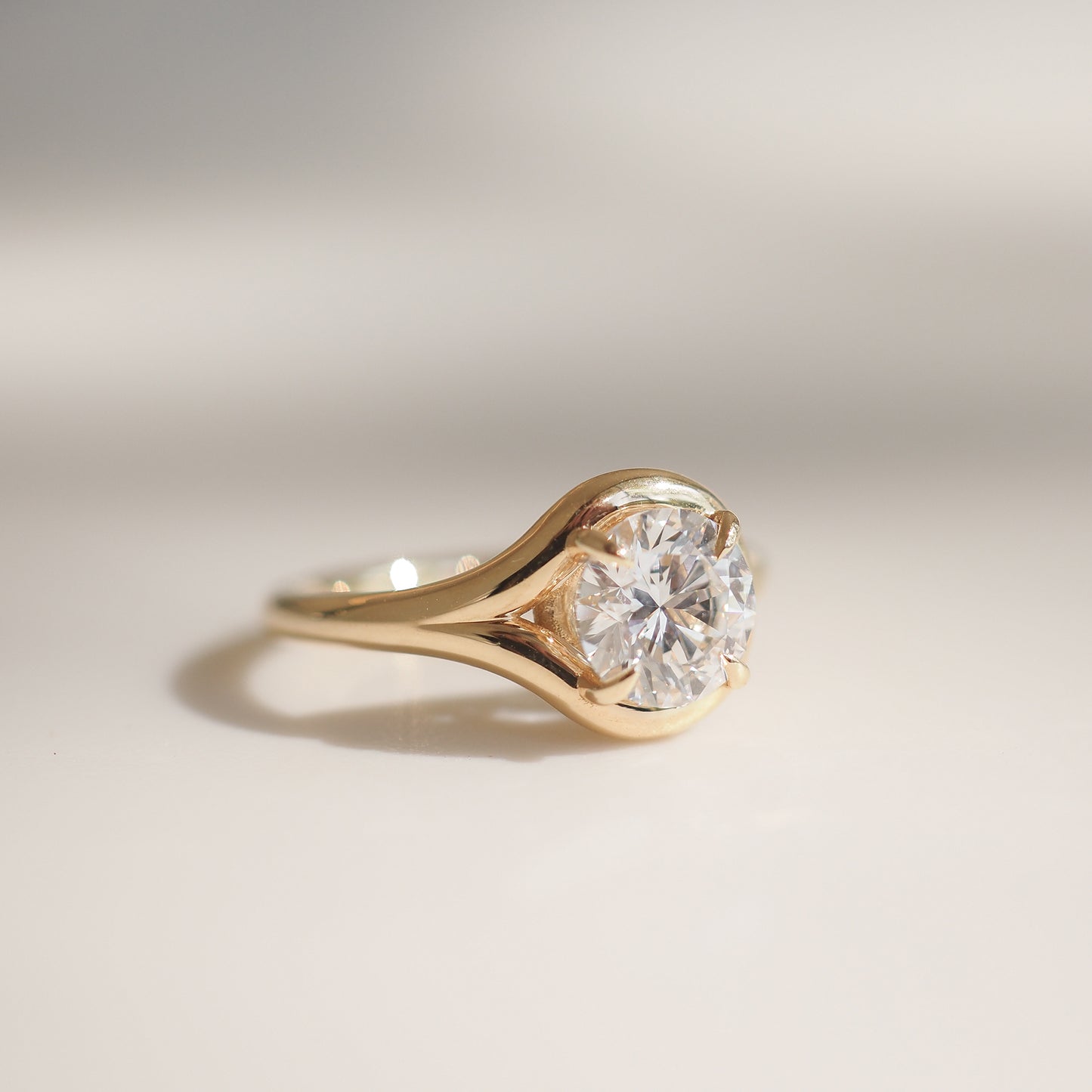 Gold ring with a large, round-cut diamond solitaire, elegantly set in a polished band, casting a subtle shadow on a light surface.