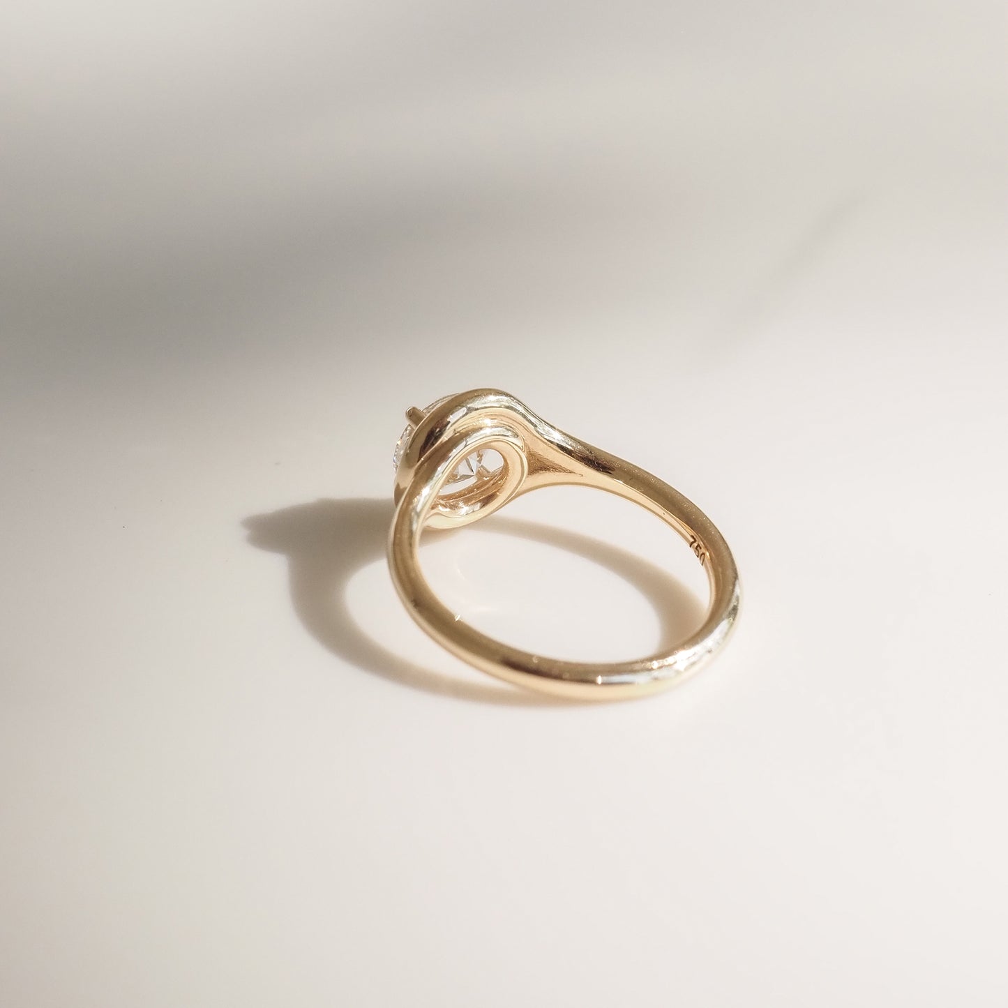 Elegant gold ring with a unique swirl setting and a solitaire diamond, casting a soft shadow on a light background.