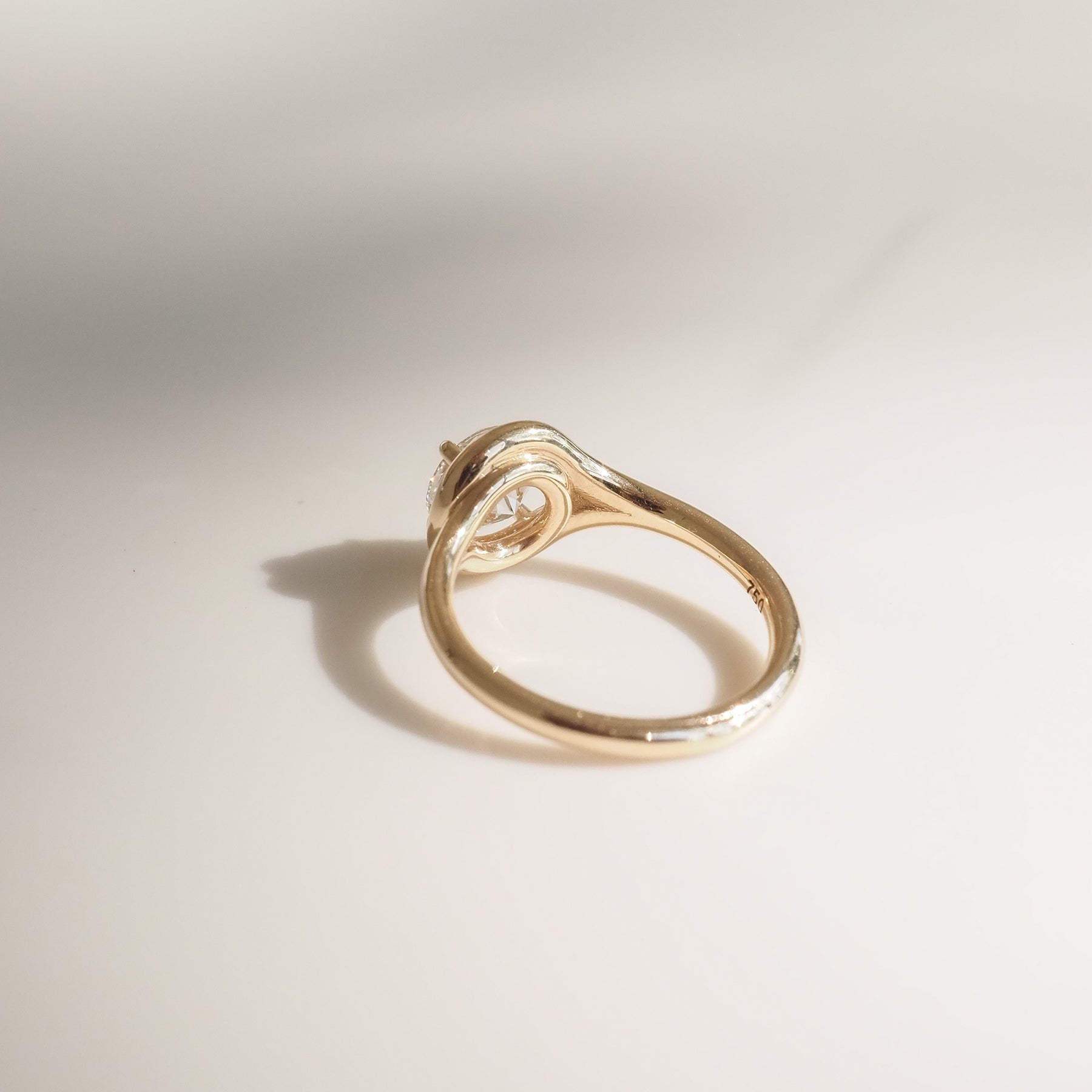 Elegant gold ring with a unique swirl setting and a solitaire diamond, casting a soft shadow on a light background.