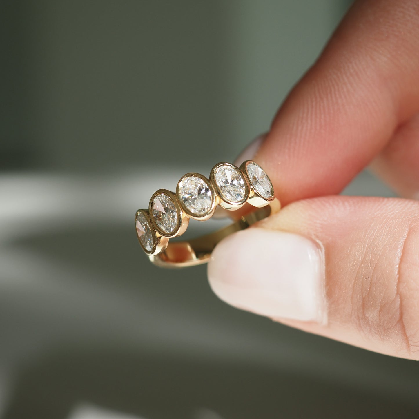 Gold ring with five oval-cut diamonds held between fingers, showcasing luxury jewellery design.