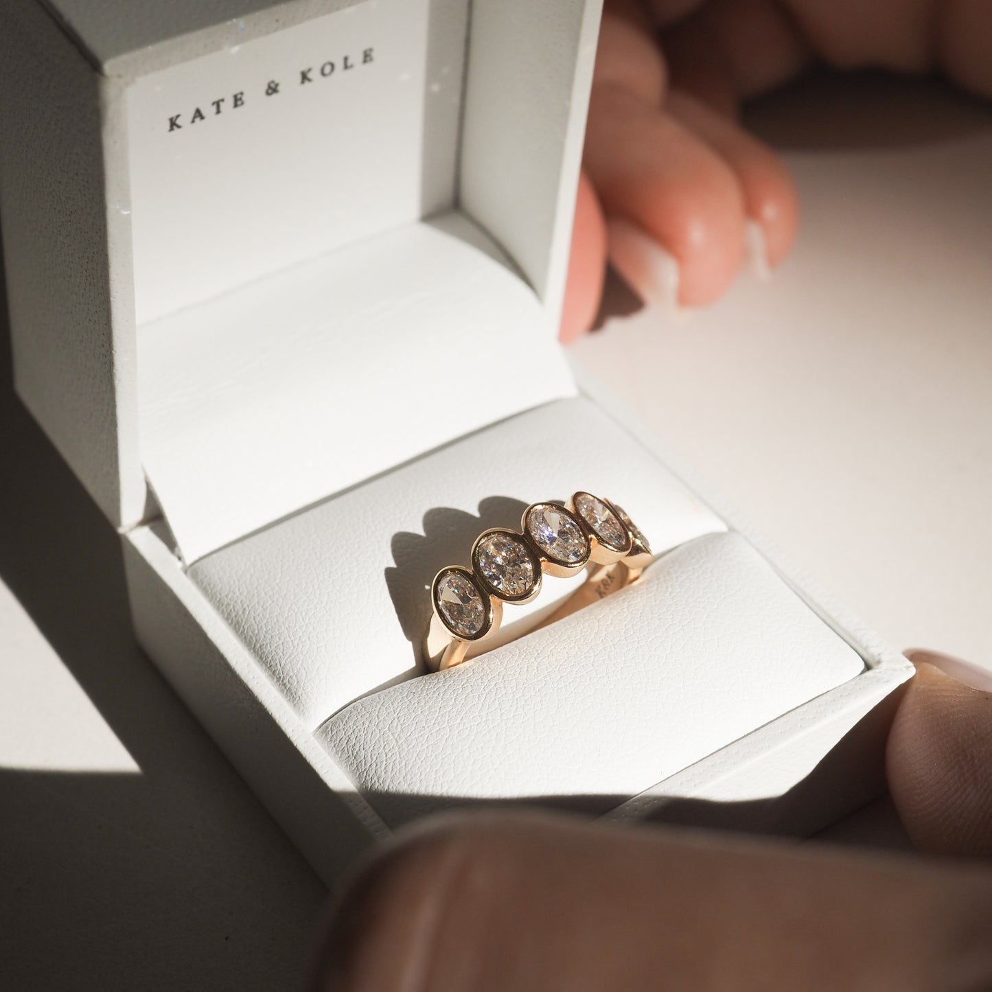 Gold ring with five oval gemstones in a Kate & Kole jewellery box, held by two hands.