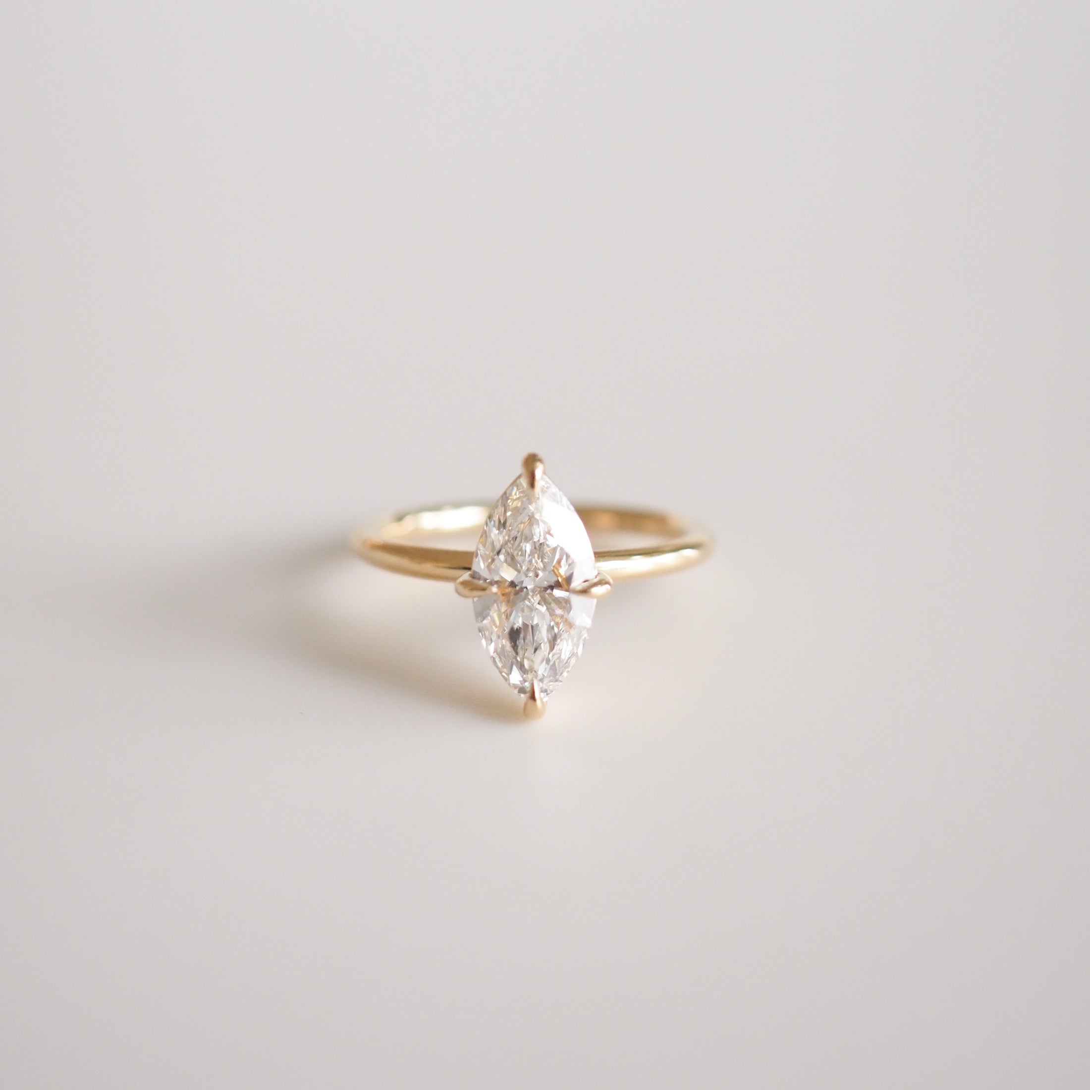 Marquise diamond ring set on a delicate gold band, resting on a soft white background. Ideal for luxury jewellery enthusiasts.