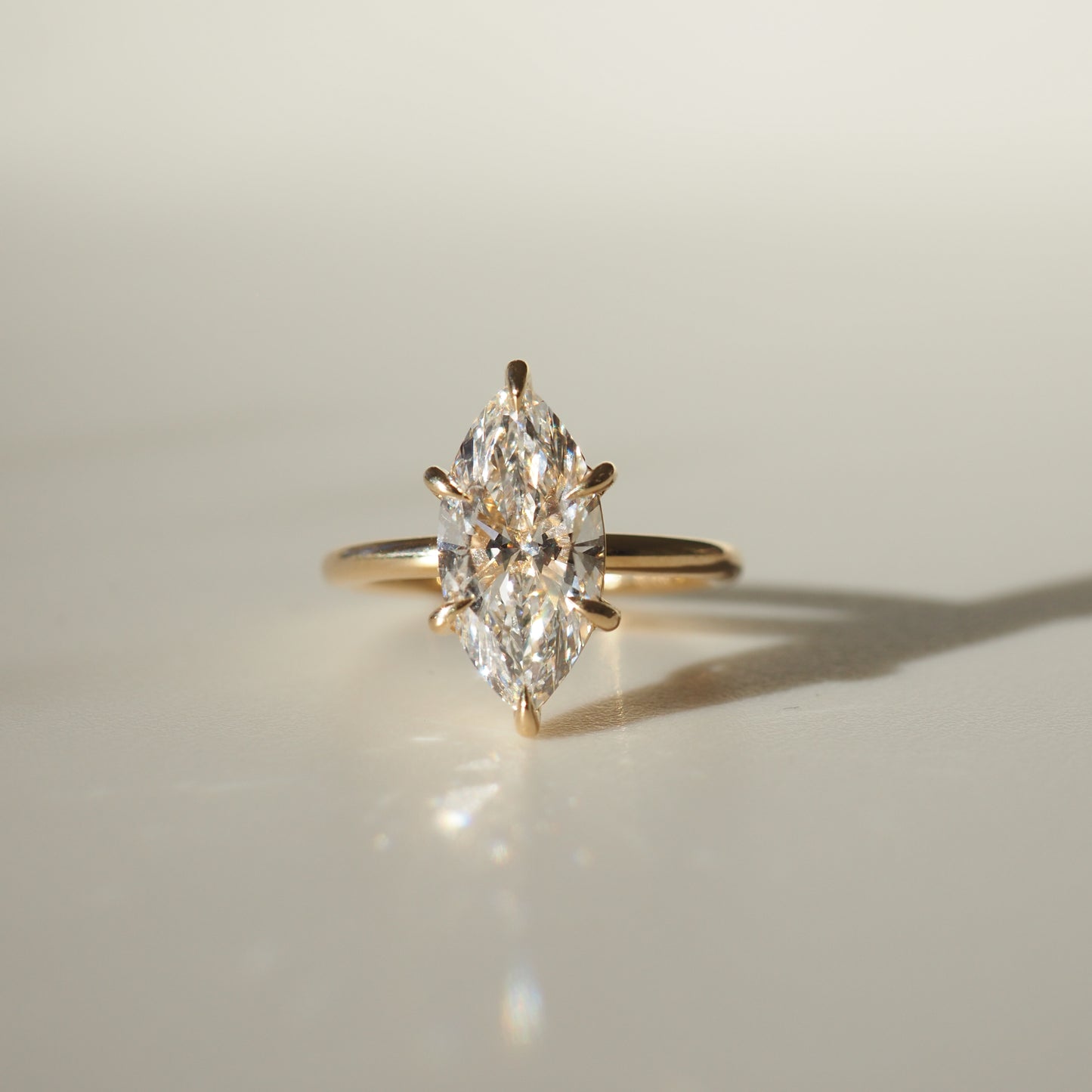 Marquise diamond ring with a gold band, elegantly displayed on a light background, casting a soft shadow; luxury jewellery.