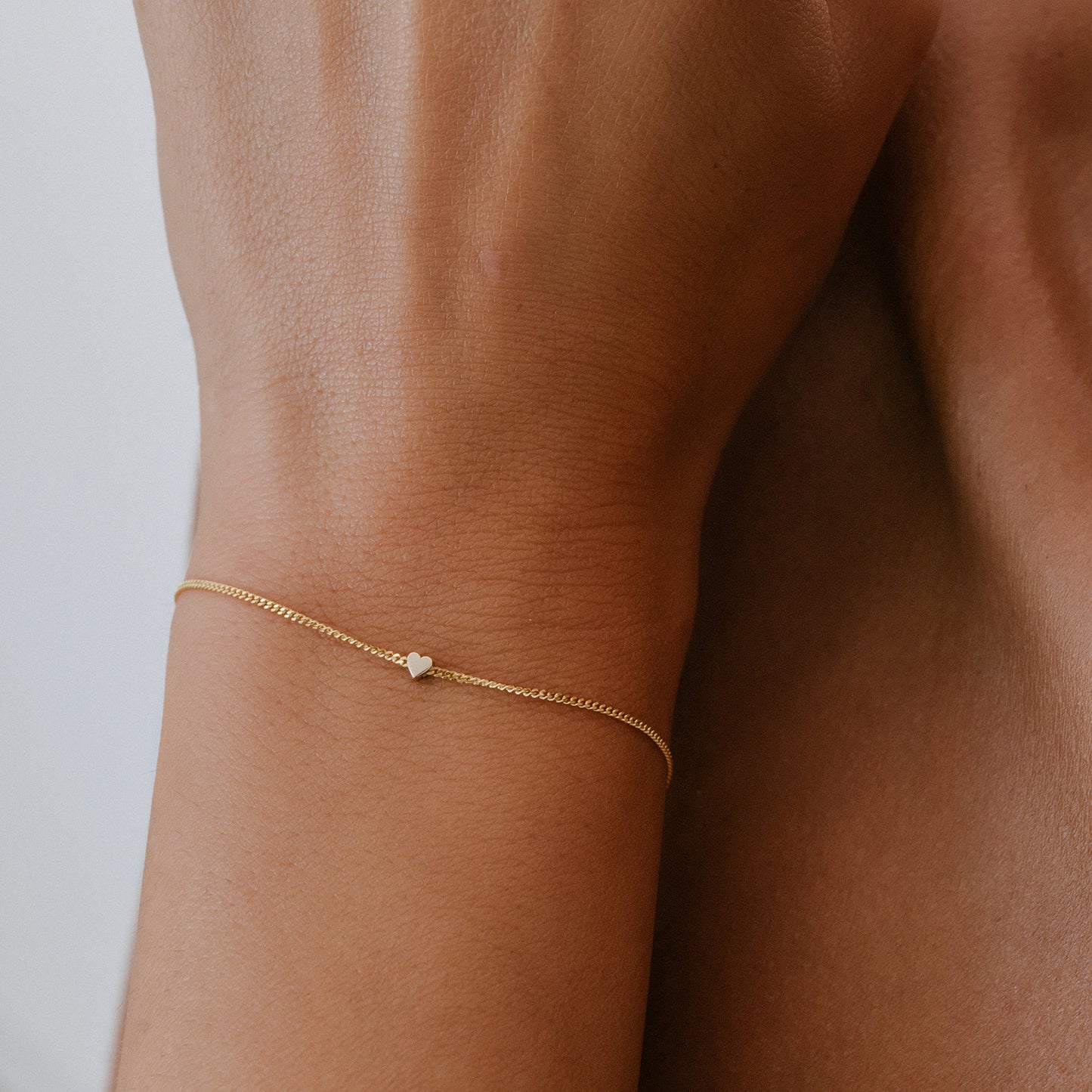 Elegant gold bracelet with a small heart charm on a woman's wrist, symbolising luxury and simplicity in jewellery design.