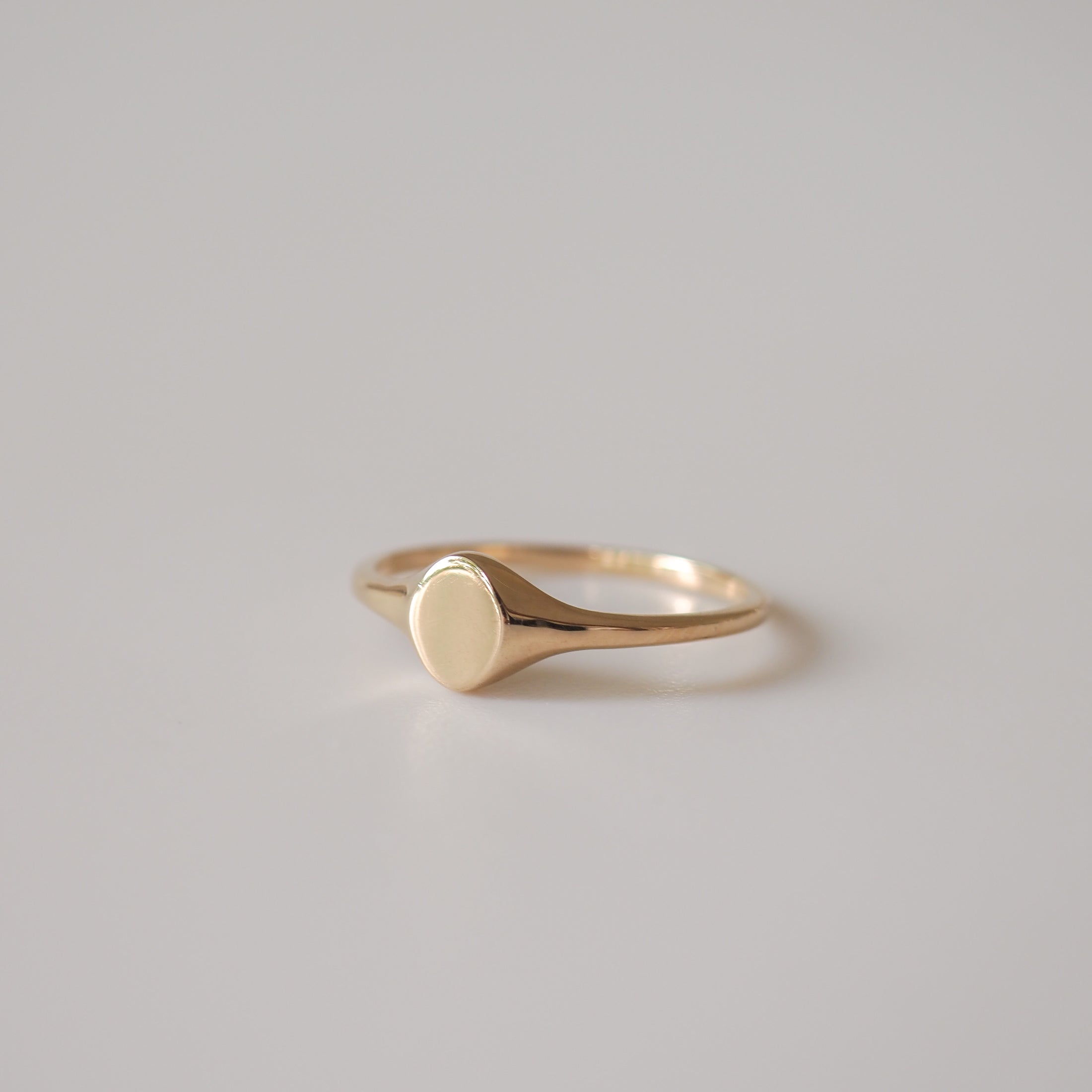 Elegant gold signet ring with a smooth, polished surface, set against a neutral grey background. Perfect for luxury jewellery collections.