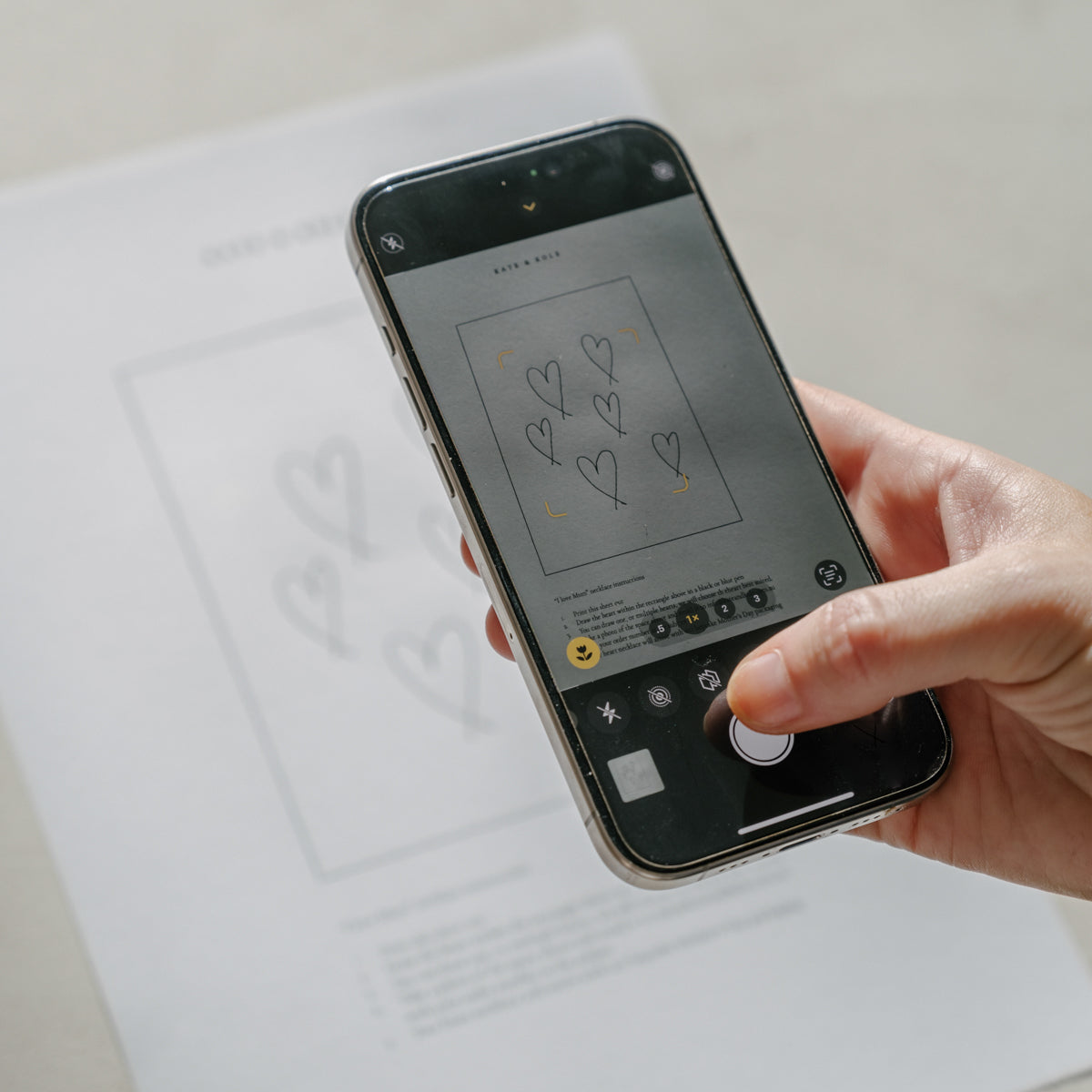 Person using a smartphone to photograph a paper with heart sketches. Modern design, creative concept capture.