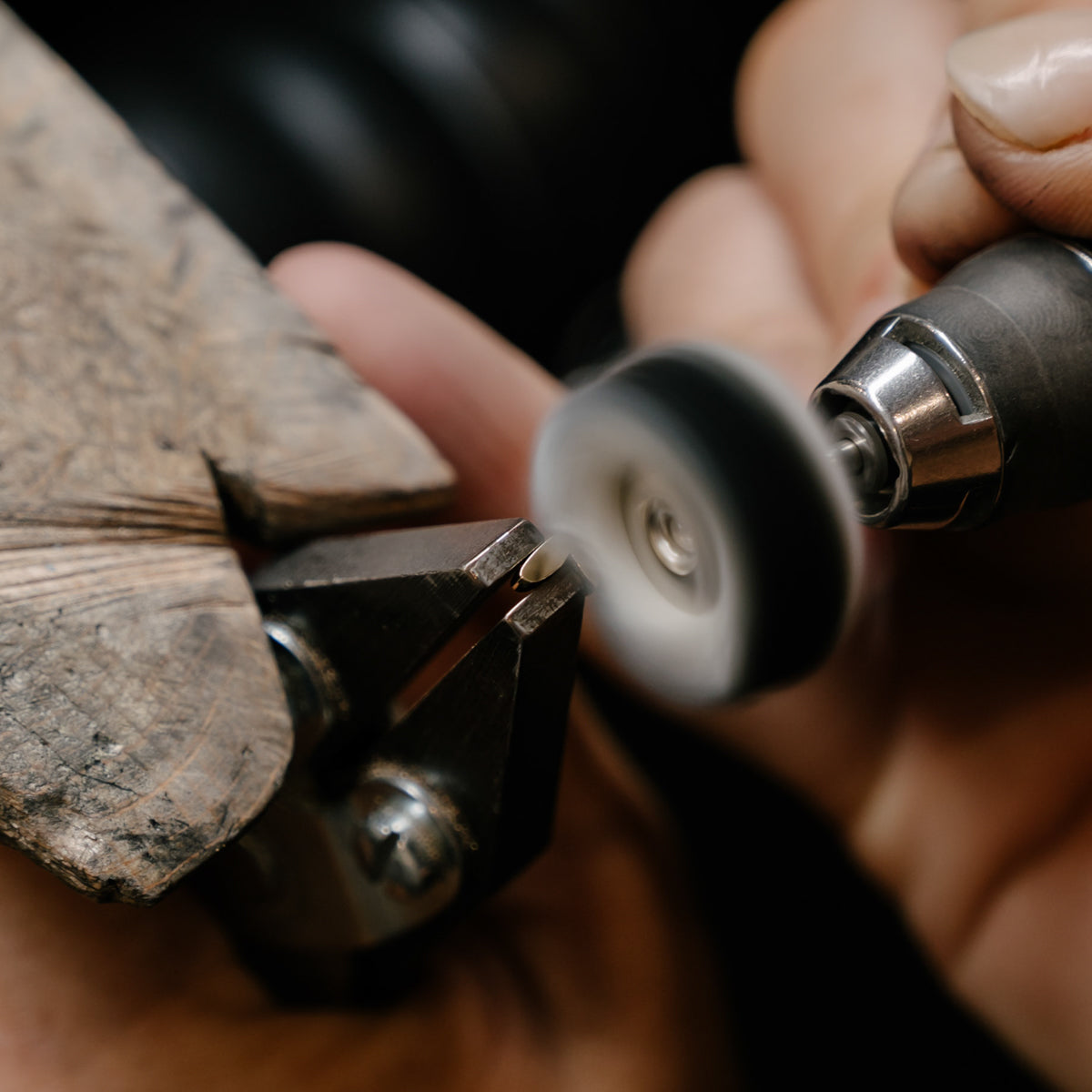 Jeweller's hands polishing a ring on a rotating tool with a wooden clamp, showcasing craftsmanship in luxury jewellery making.