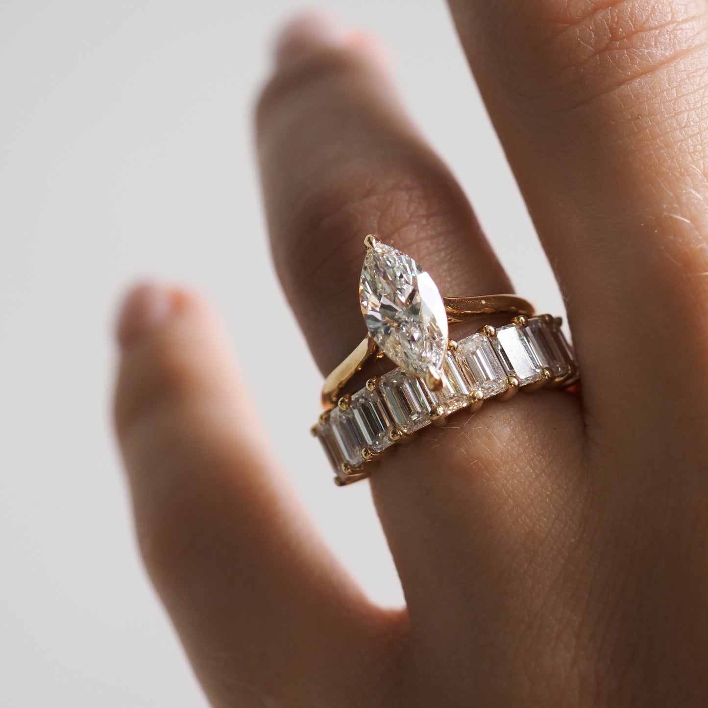 Close-up of a hand wearing a marquise-cut diamond ring atop a gold band with emerald-cut diamonds, symbolising luxury and elegance.